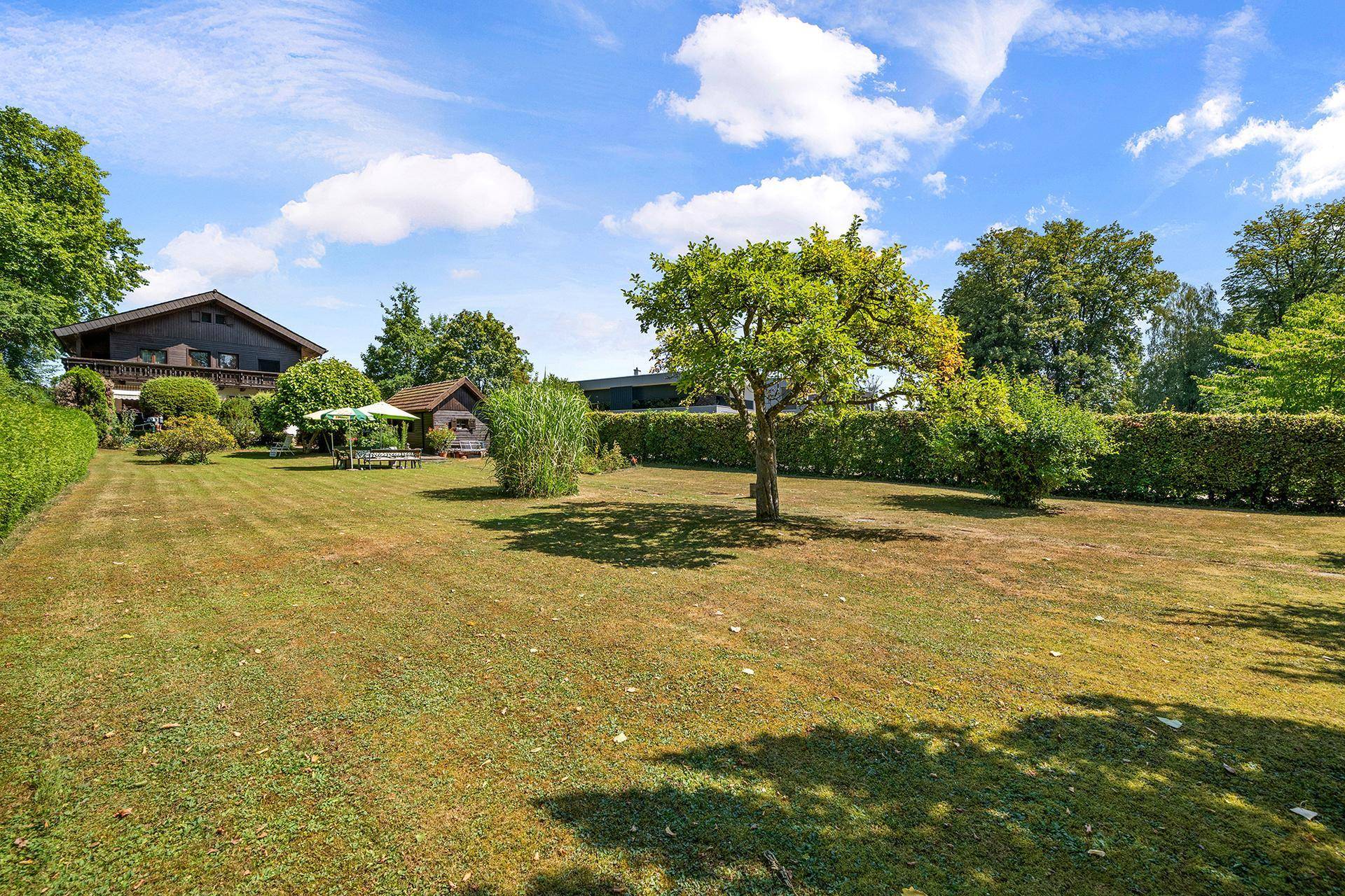 Ausgedehnter Garten mit Rasenfläche, Obstbäumen und einem traditionellen Chalet im Hintergrund.