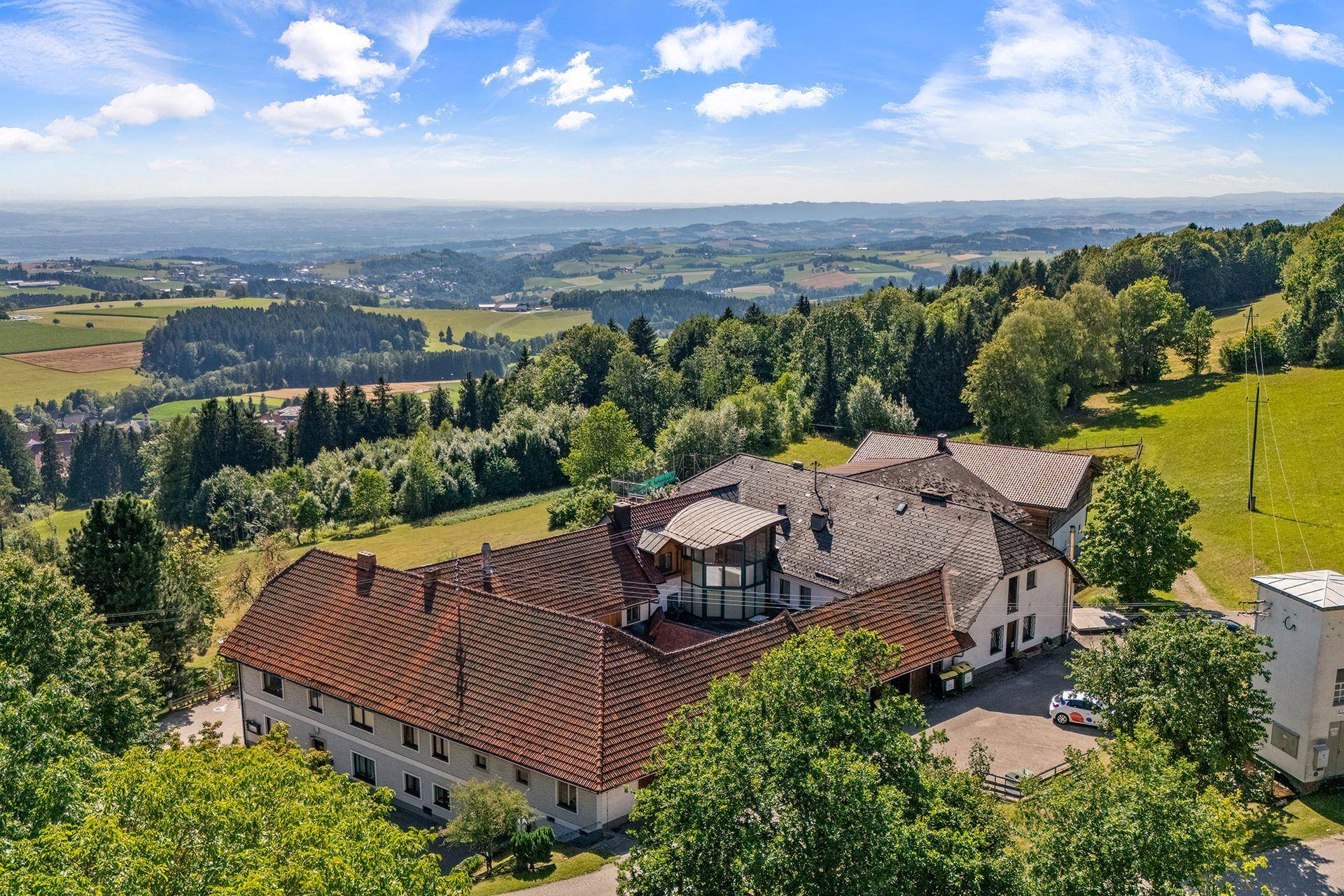 Panoramablick aus der Vogelperspektive auf das Anwesen und die weite, hügelige Landschaft mit Wäldern.