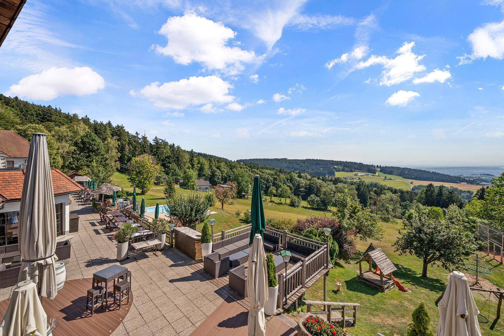 Große Außenterrasse mit verschiedenen Sitzbereichen, Sonnenschirmen und Blick auf die Landschaft.