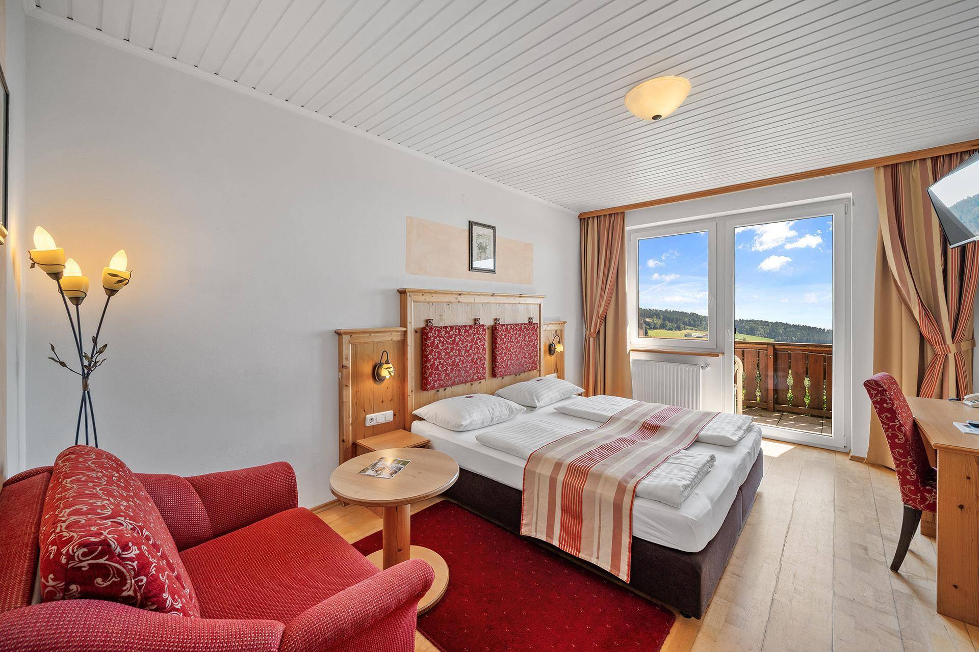 Helles Schlafzimmer mit Doppelbett, rotem Sessel und Zugang zu einem Balkon mit schöner Aussicht.