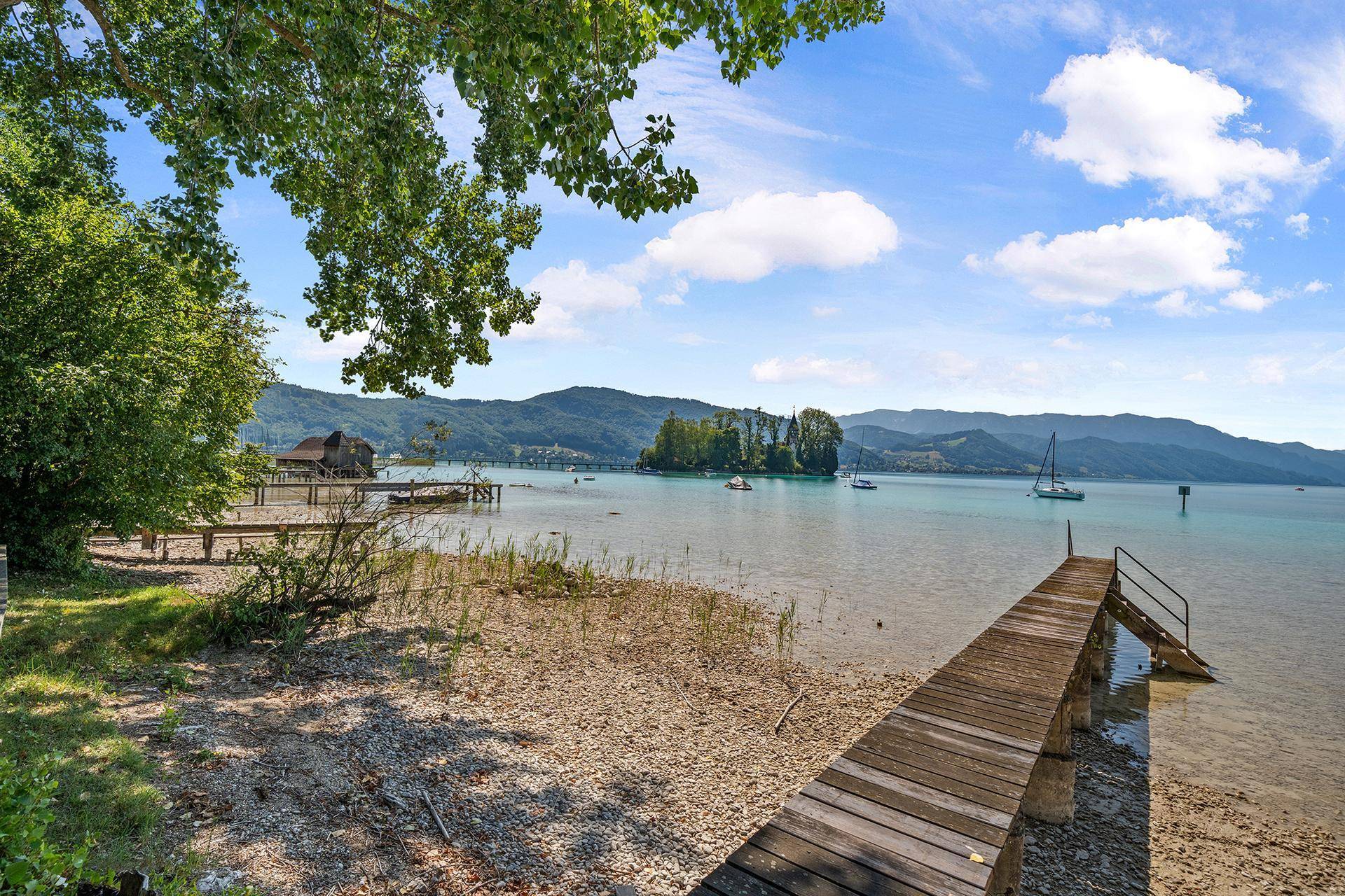 Holzsteg am Ufer des Sees mit Blick auf die umliegende Natur und Segelboote.
