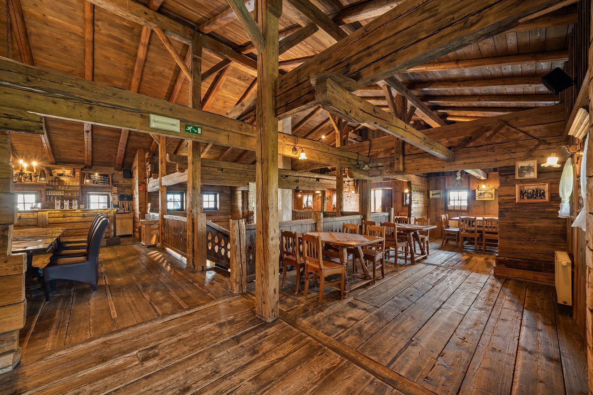 Großer, rustikaler Gastraum mit Holzböden, Holzbalken und vielen Tischen in traditionellem Ambiente.
