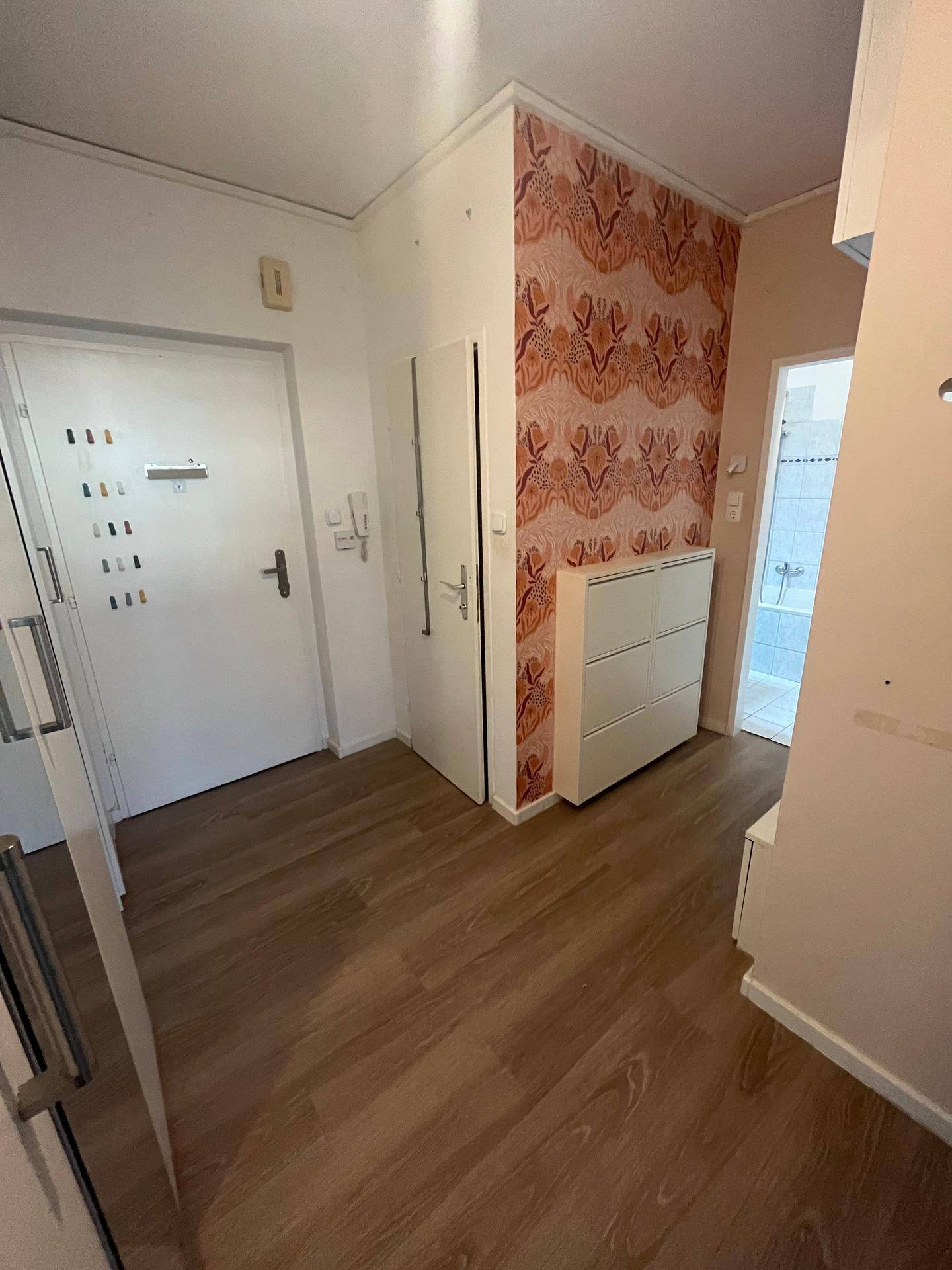 Eingangsbereich mit gemusterter Tapete, Schuhschrank und Zugang zu weiteren Räumen.