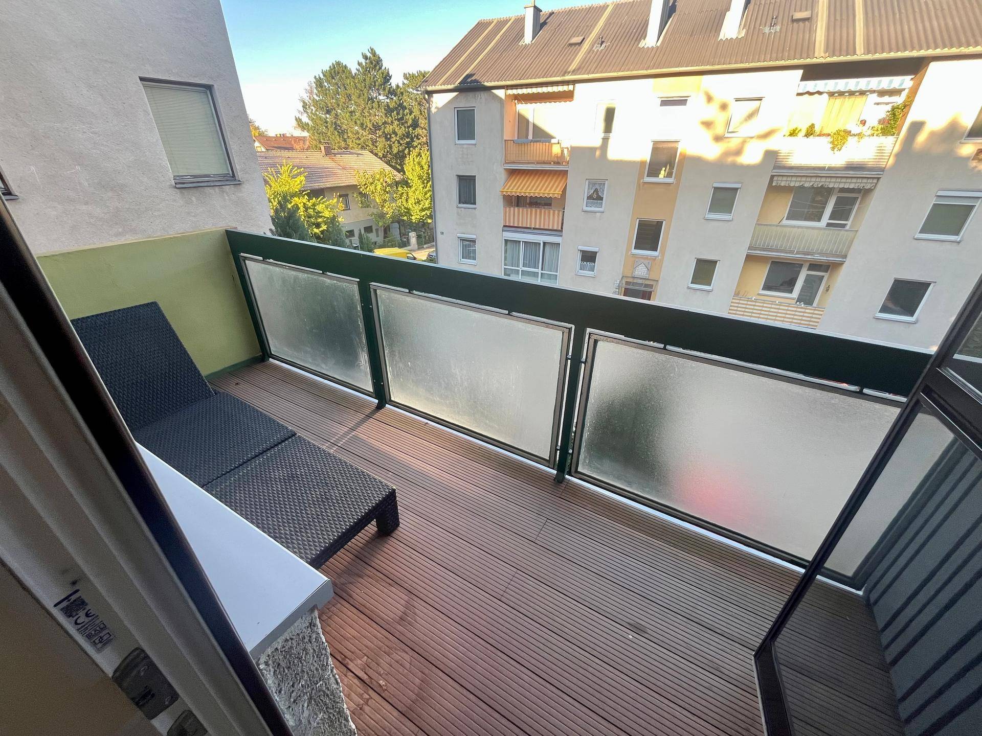 Balkon mit Holzboden und Liegestuhl, bietet einen Blick auf die umliegenden Gebäude.