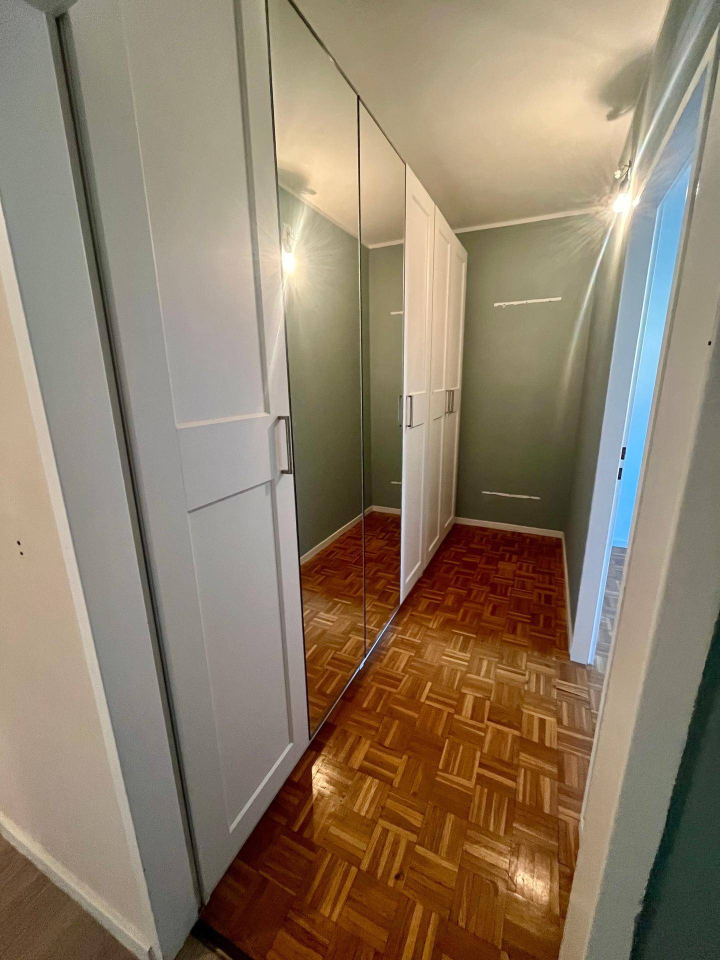 Langer Flur mit Spiegelschränken und Laminatboden, der zu weiteren Zimmern führt.