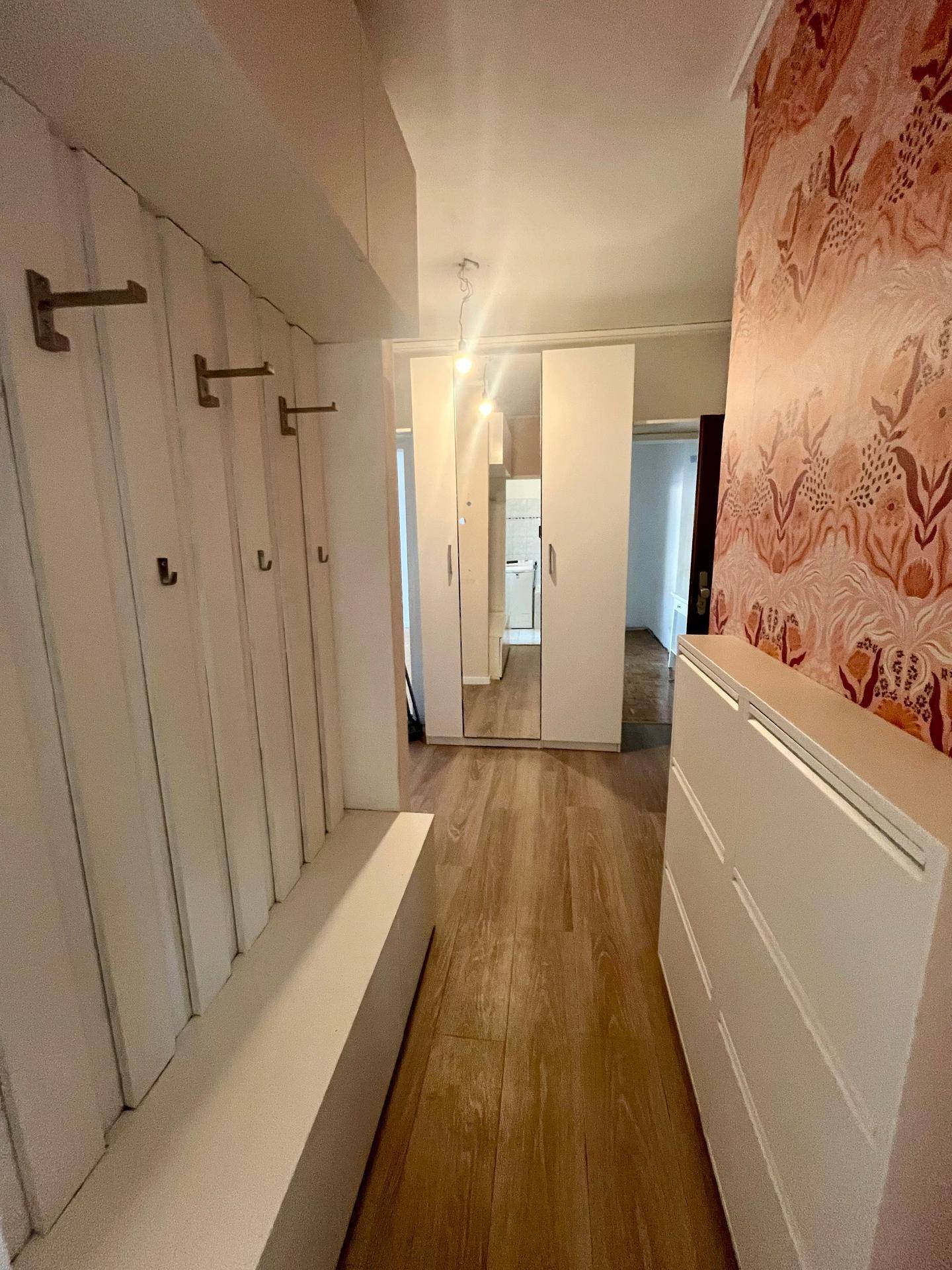 Heller Eingangsbereich mit Garderobe, Sitzbank und gemusterter Tapete, einladend gestaltet.