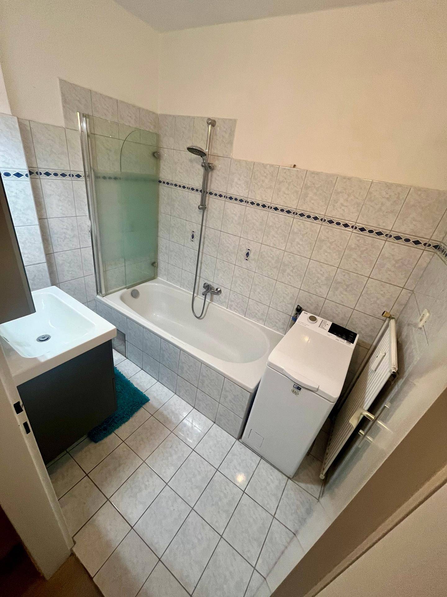 Badezimmer mit Badewanne, Duschvorrichtung, Waschbecken und Fliesen an Wänden und Boden.