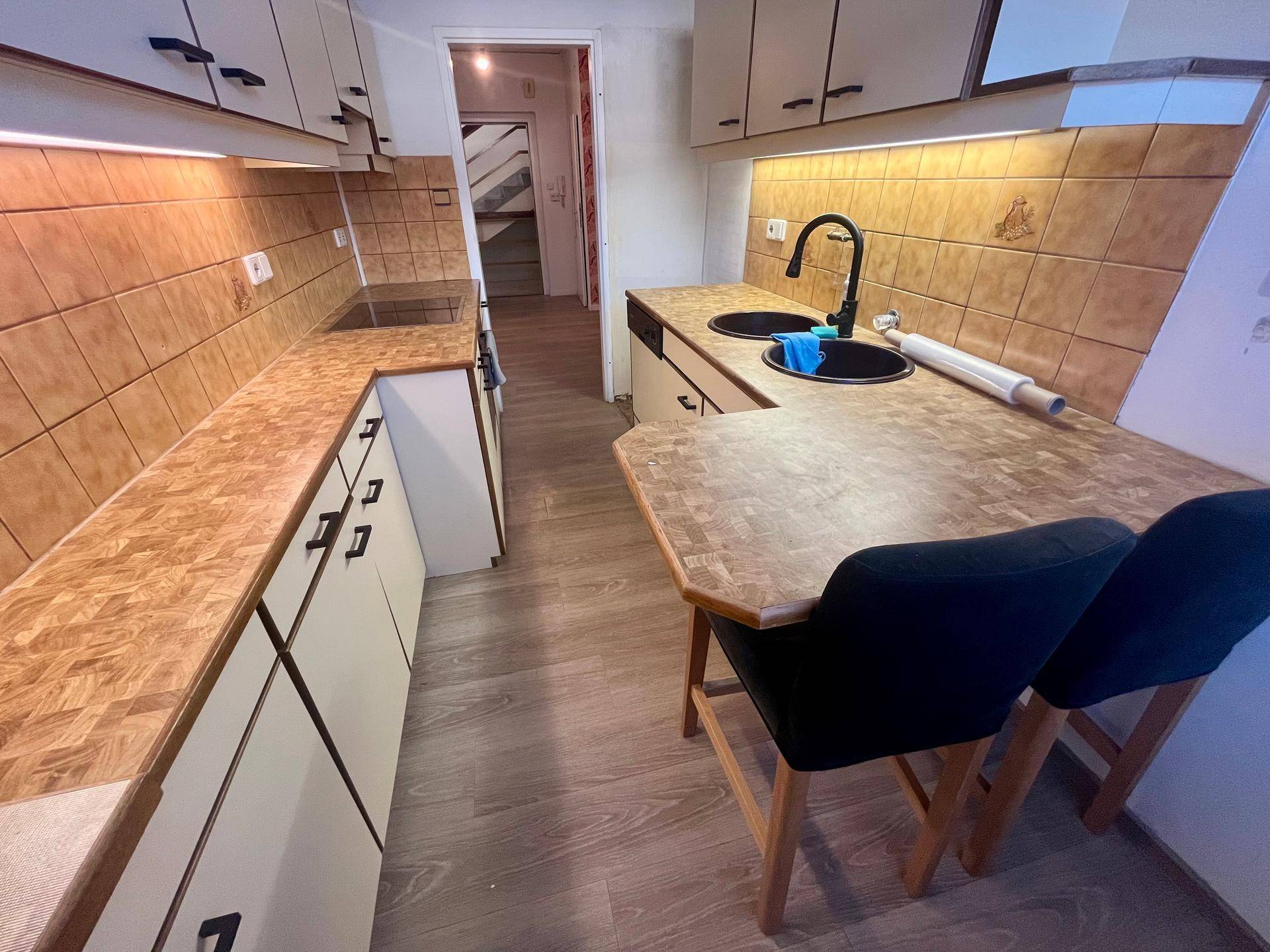 Küche mit beigen Fliesen, Holzoptik-Arbeitsplatten und integriertem Essbereich.