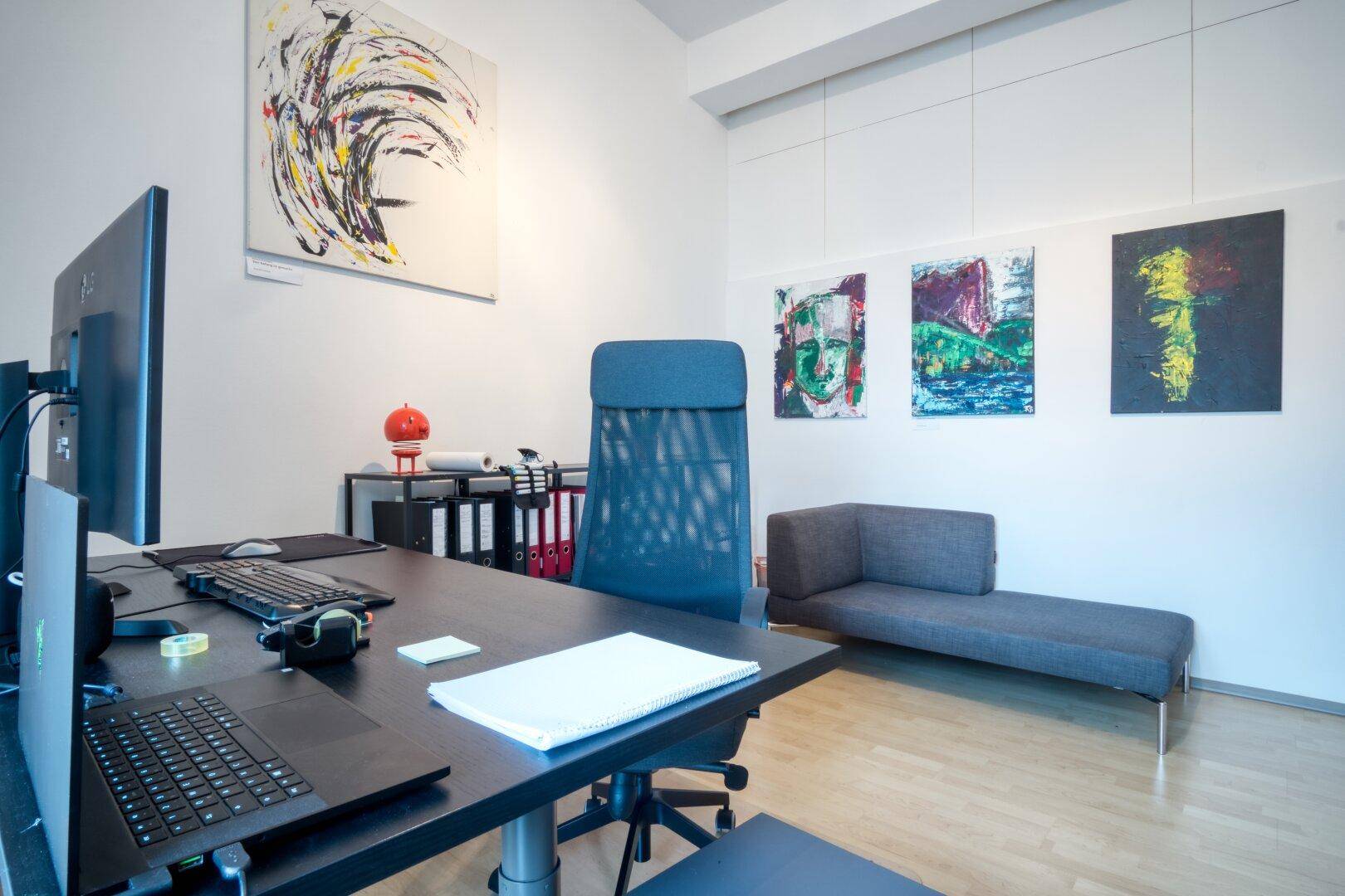 Moderner Büroraum mit großem Schreibtisch, Laptop, ergonomischem Stuhl und einer stilvollen Chaiselongue.