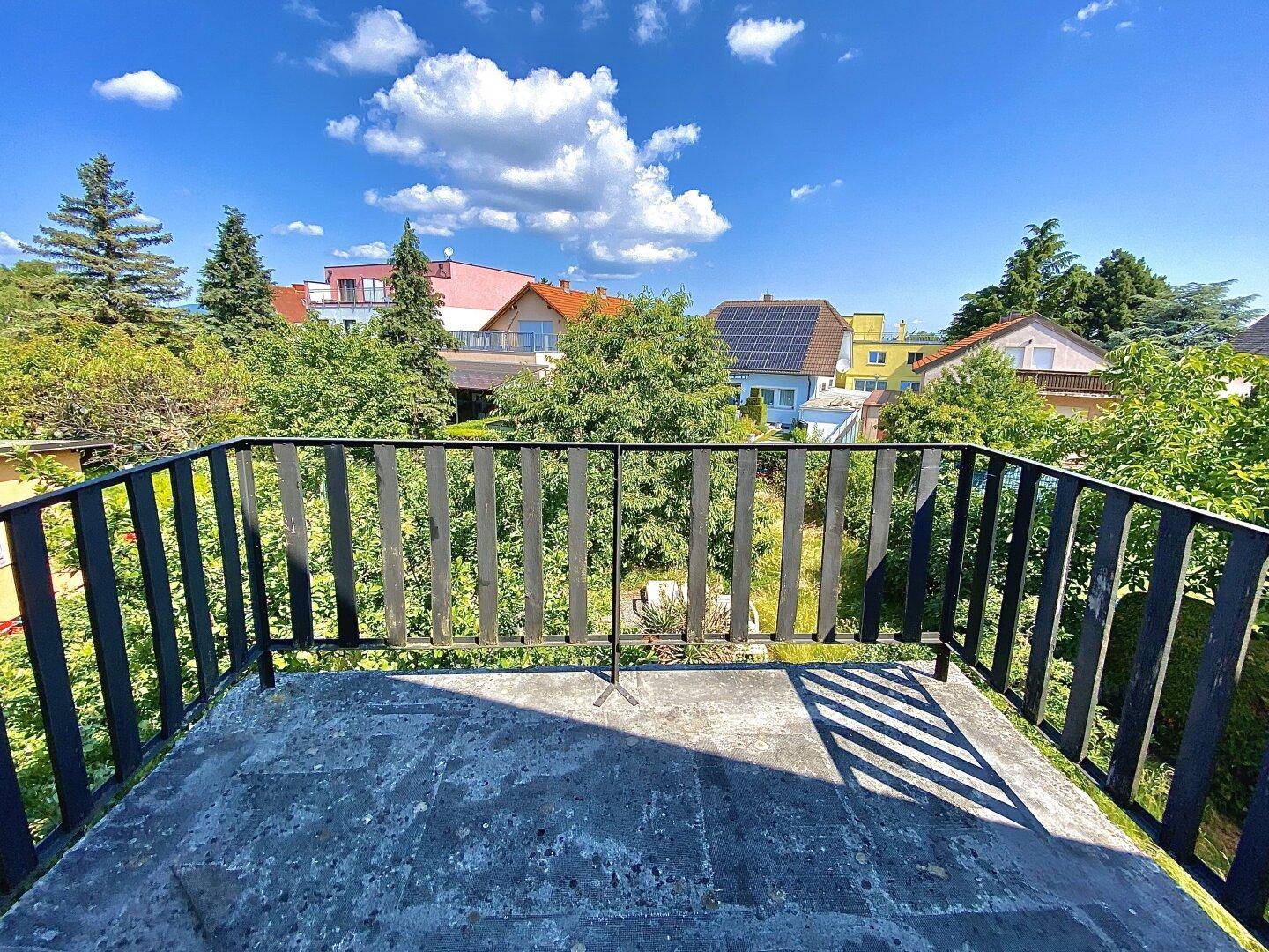 Blick vom Balkon auf die umliegende Wohngegend mit viel Grün und weiteren Häusern.