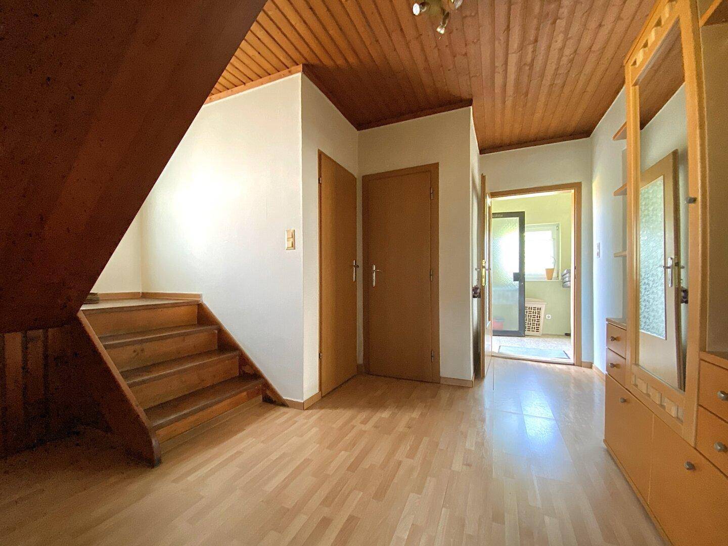 Heller Flur mit Holztreppe, Holzboden und Holzdecke, der zu weiteren Räumen führt.