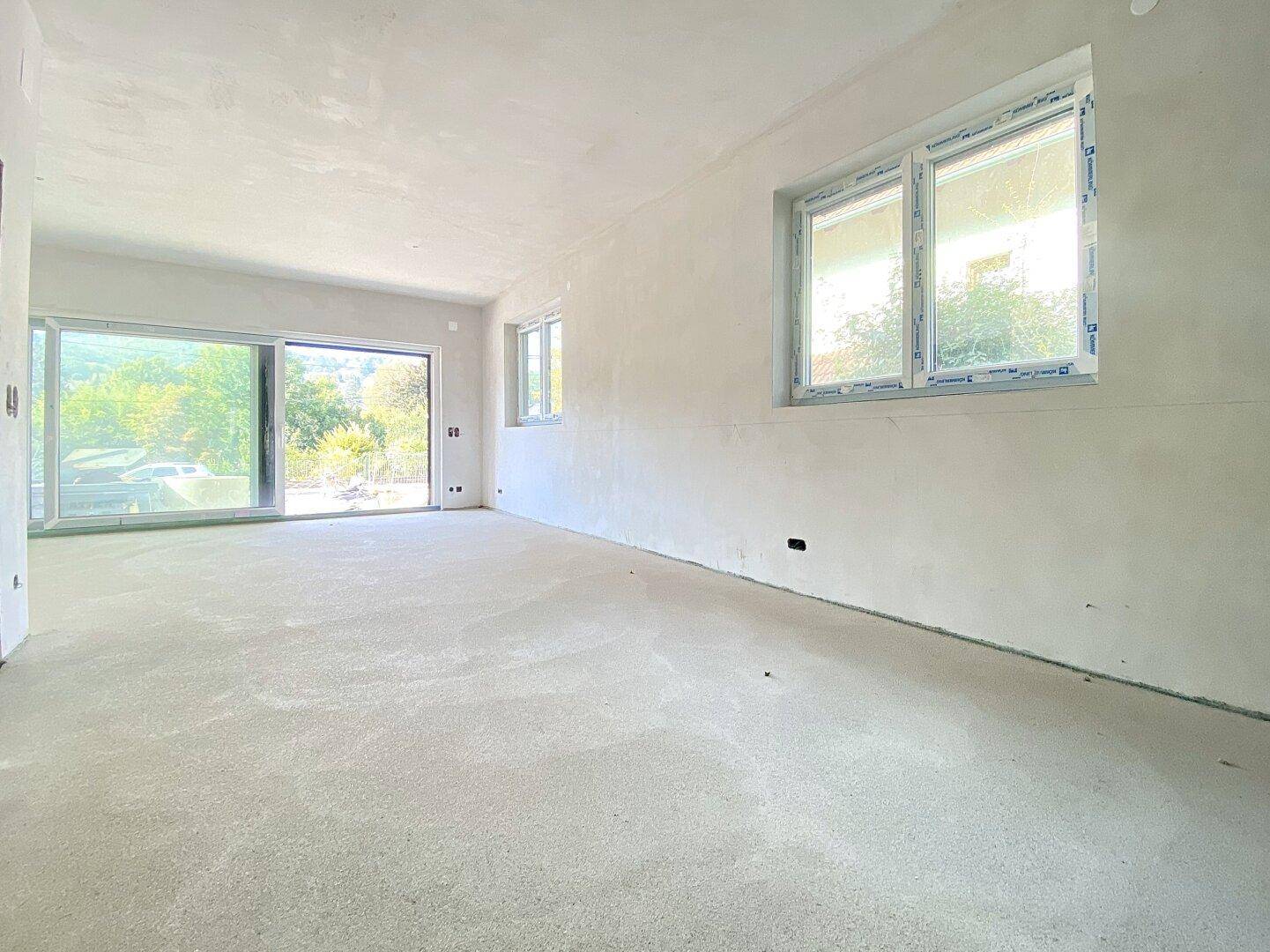 Heller, unfertiger Raum mit großen Fenstern, die viel Tageslicht hereinlassen.