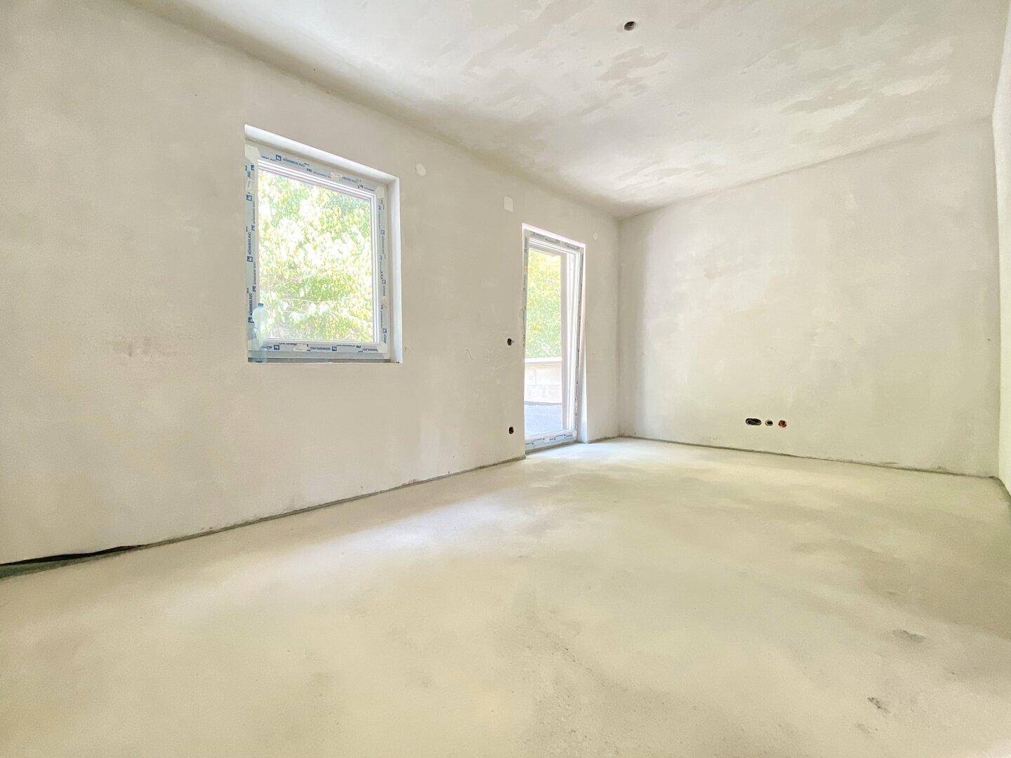 Unfertiger Raum mit Fenster und Zugang nach draußen, ideal für zukünftige Wohnbereiche.