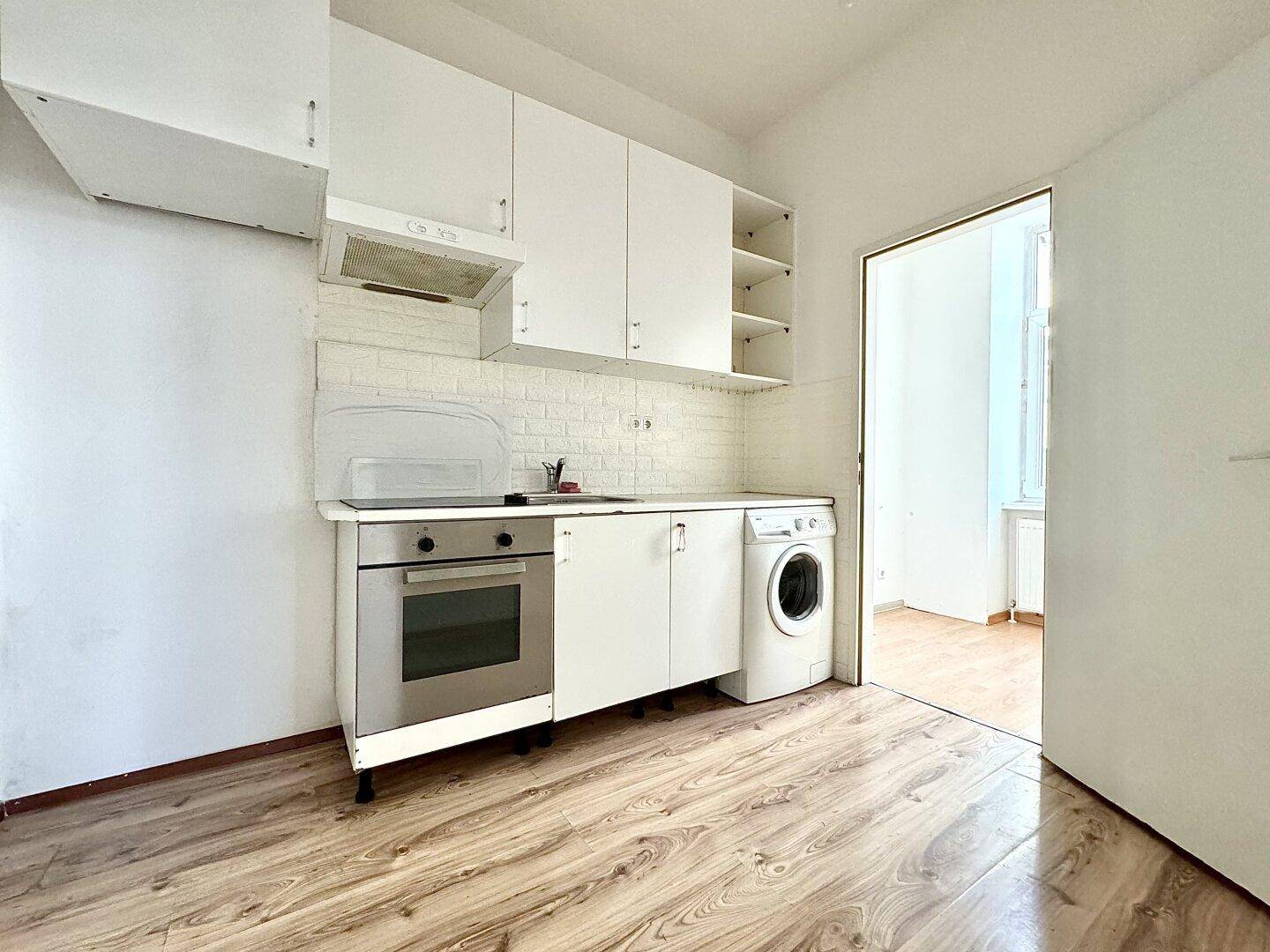 Kompakte Einbauküche mit weißen Schränken, Backofen und integrierter Waschmaschine.