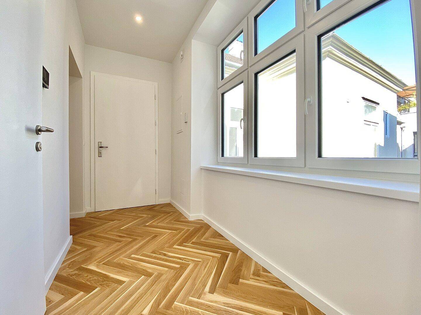 Heller Eingangsbereich mit Fischgrätparkettboden und großem Fenster, das viel Tageslicht hereinlässt.