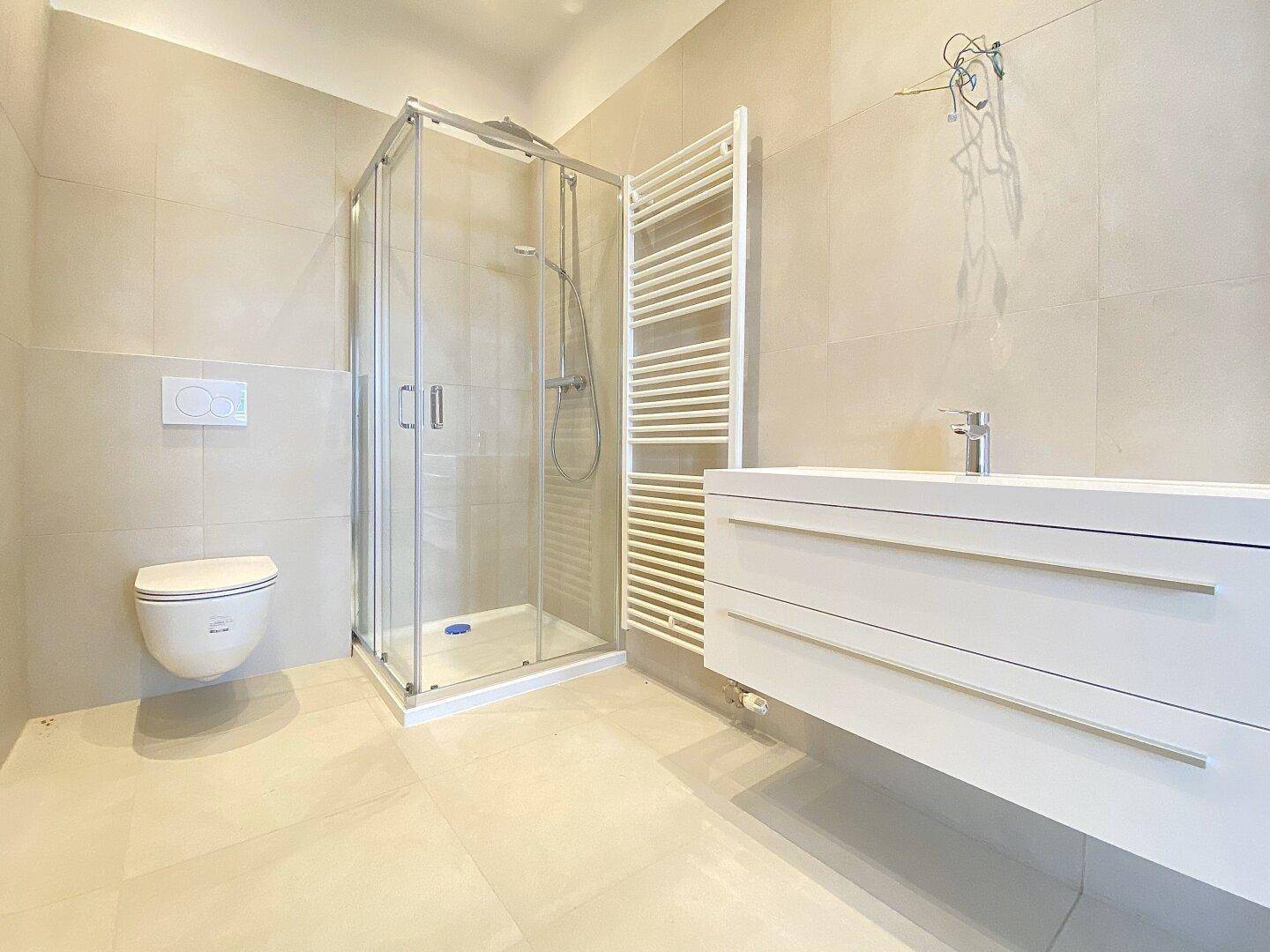 Modernes Badezimmer mit begehbarer Dusche, wandhängendem WC und beheiztem Handtuchhalter, in hellen Fliesen.