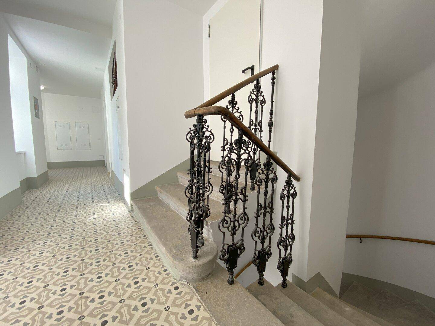 Historisches Treppenhaus mit kunstvollem schmiedeeisernem Geländer und gemustertem Fliesenboden.