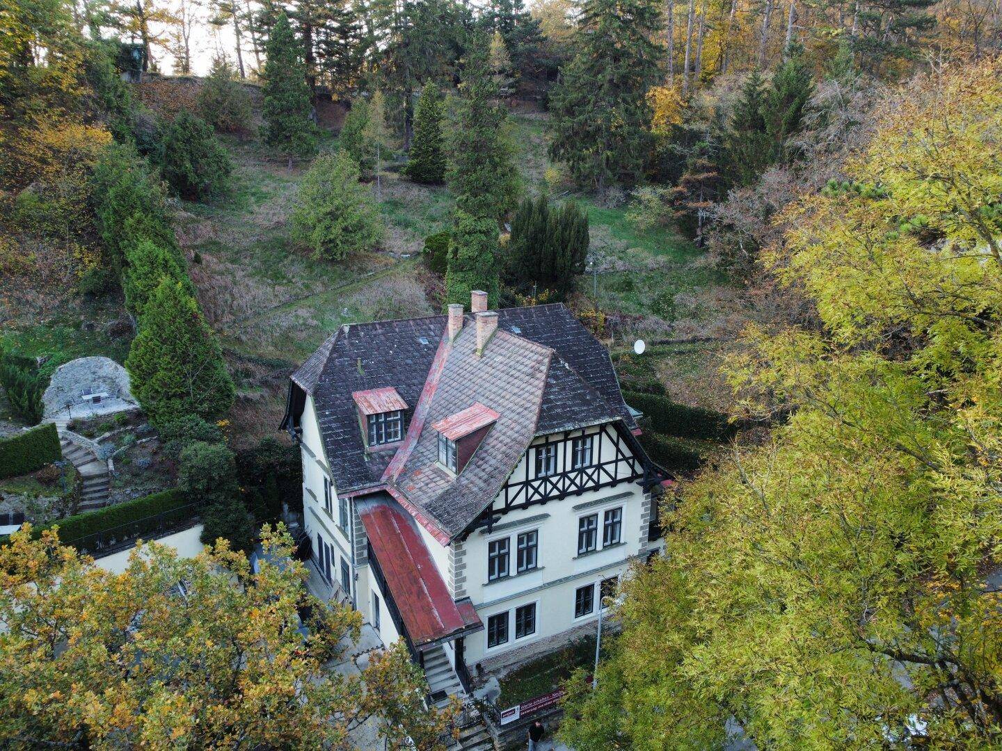 Historisches Haus mit Fachwerkdetails und Satteldach, eingebettet in eine bewaldete Hügellandschaft.