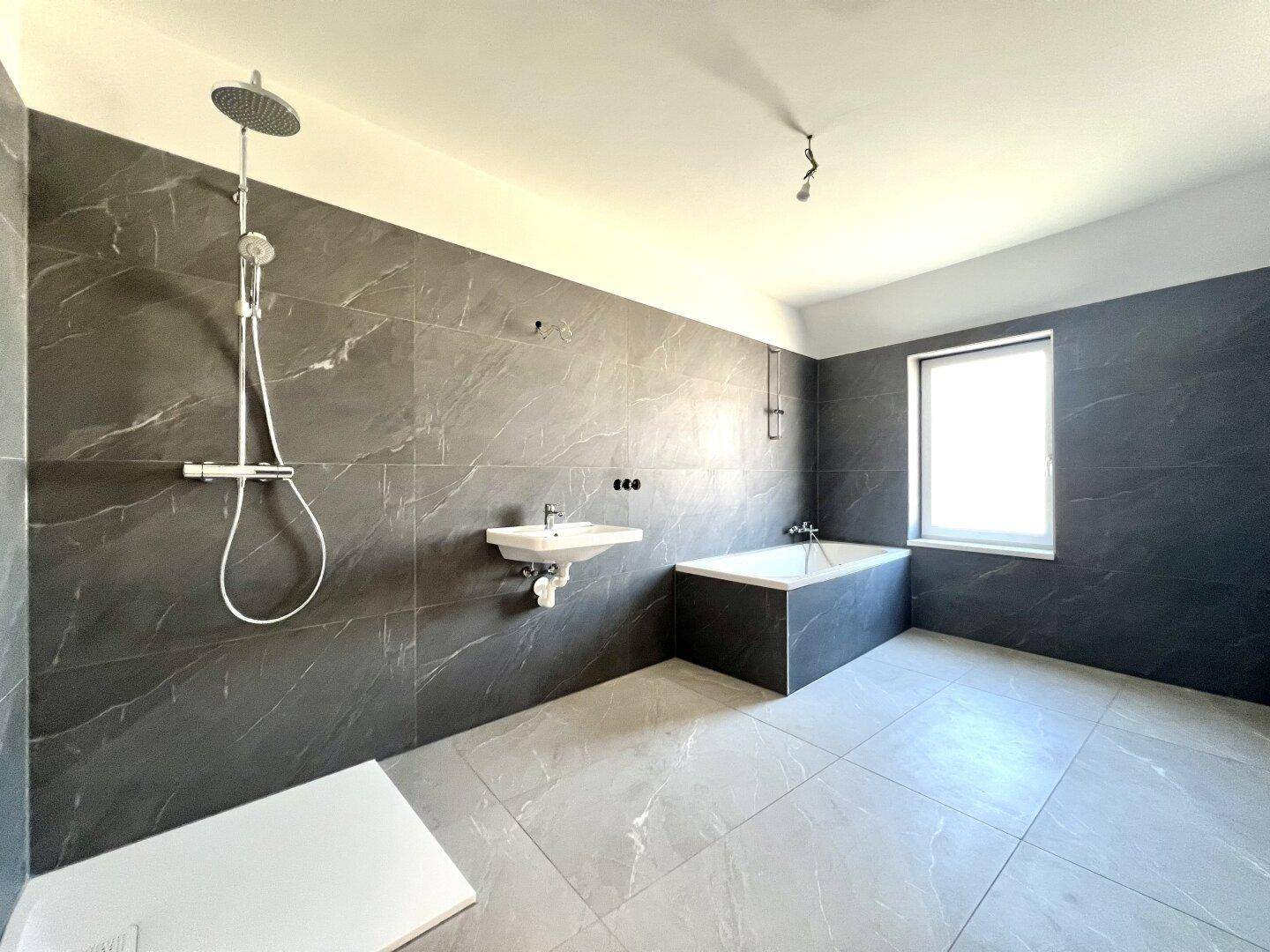 Modernes Badezimmer mit großformatigen grauen Fliesen, Badewanne und ebenerdiger Dusche.