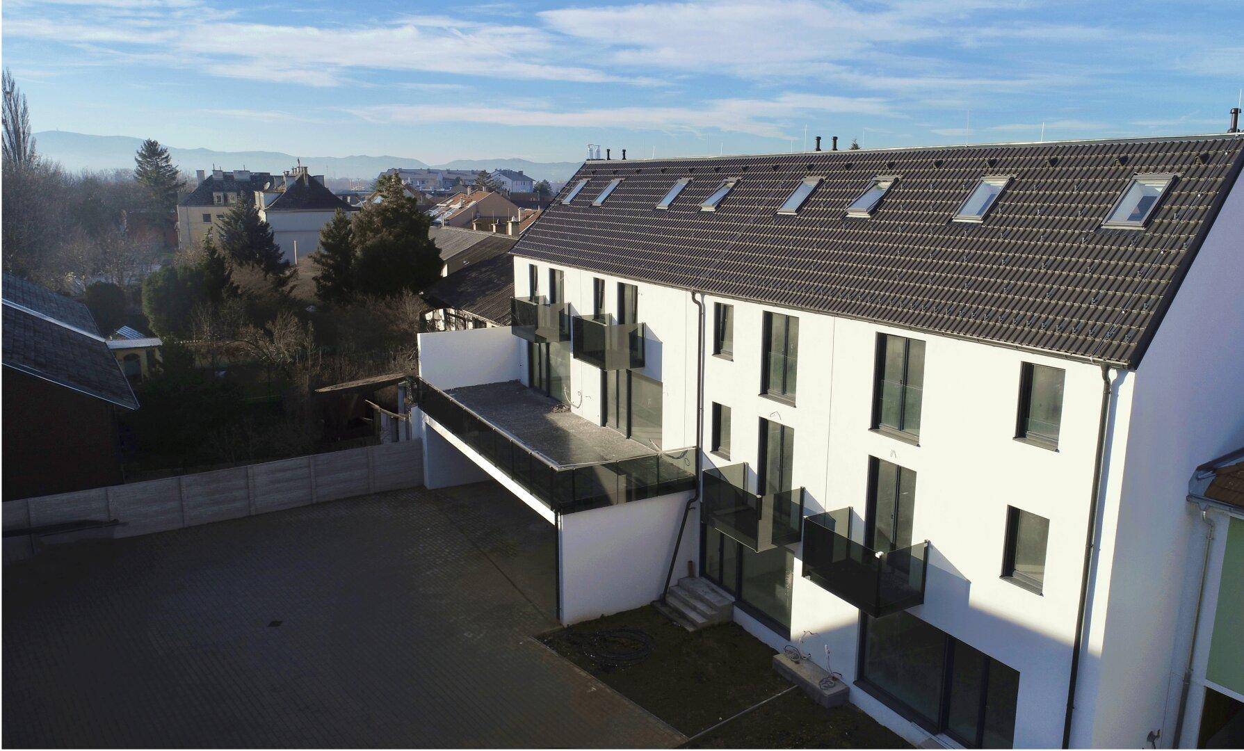 Luftaufnahme eines modernen Neubaukomplexes mit mehreren Balkonen und Dachfenstern.