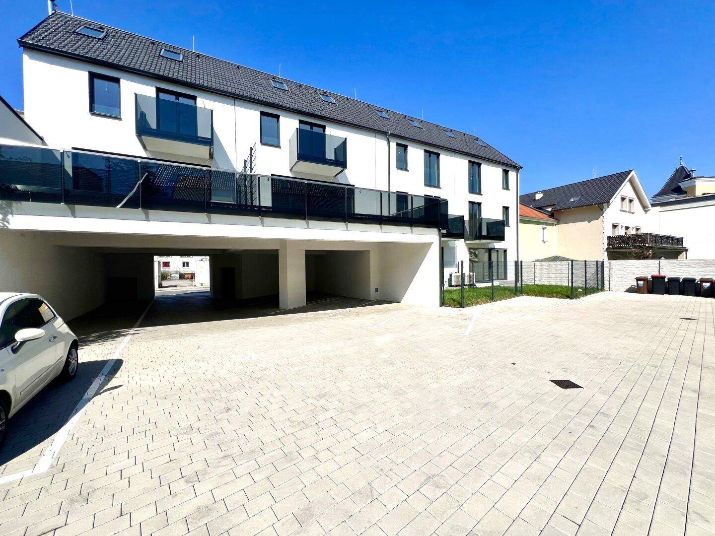 Moderne Wohnanlage mit Tiefgaragenzufahrt und gepflasterten Außenparkplätzen.