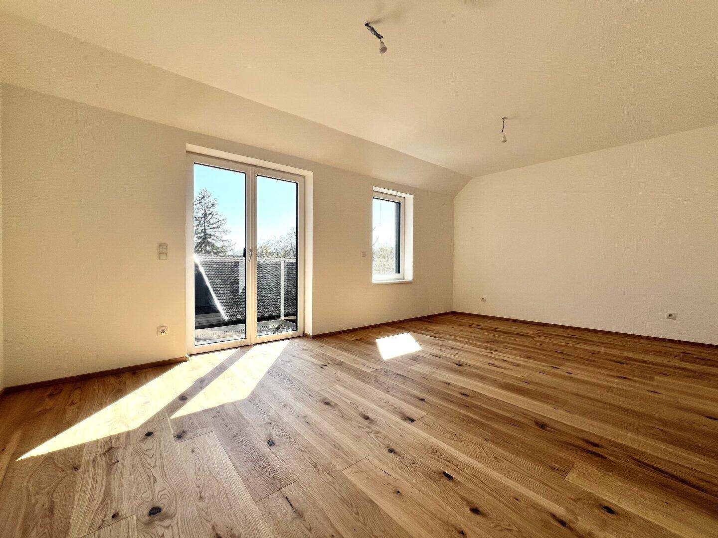 Helles Schlafzimmer mit Parkettboden und Zugang zu einem kleinen Balkon mit Aussicht.