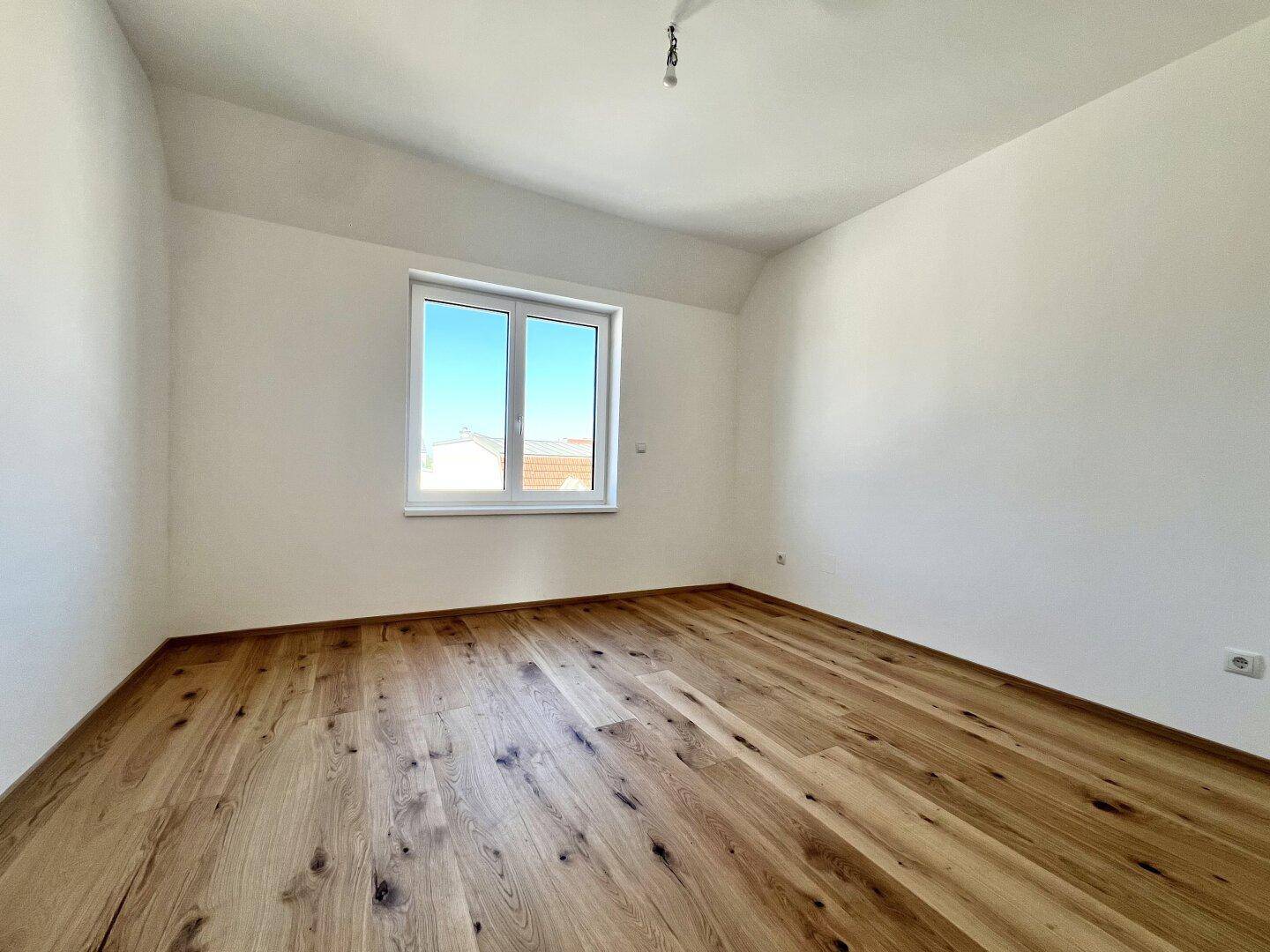 Geräumiges Schlafzimmer mit Parkettboden und Fenster, das einen angenehmen Blick ins Grüne bietet.