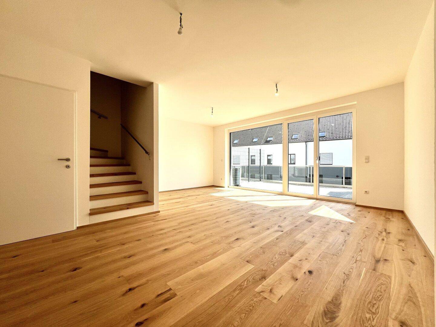 Heller Wohnbereich mit offener Holztreppe und Zugang zu einer großen Außenterrasse.