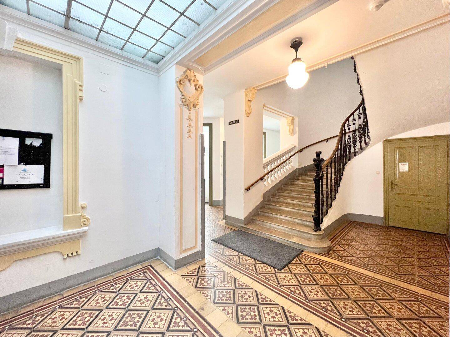 Historischer Eingangsbereich mit kunstvollen Fliesen, Treppe und Oberlicht, strahlt Charme aus.
