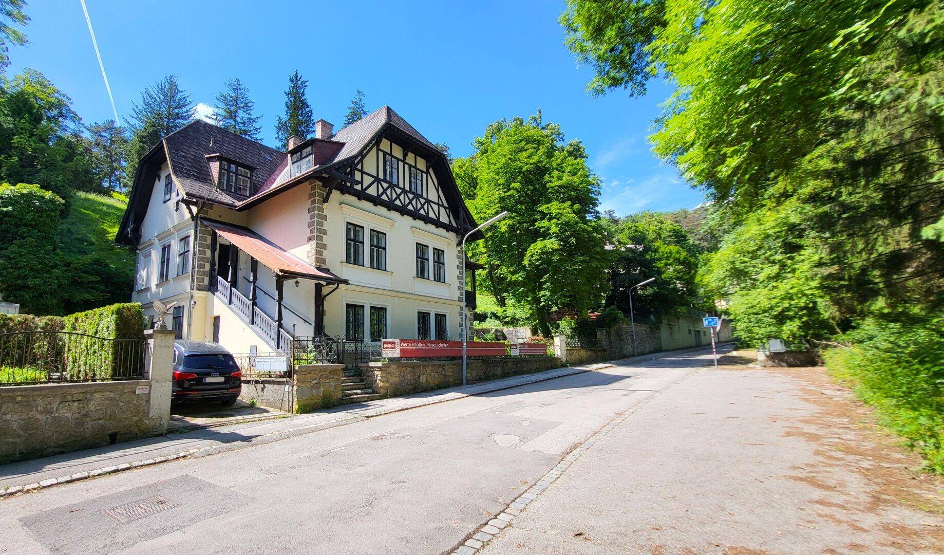 Historische Villa mit Fachwerkfassade und Satteldach, umgeben von üppigem Grün und Bäumen.