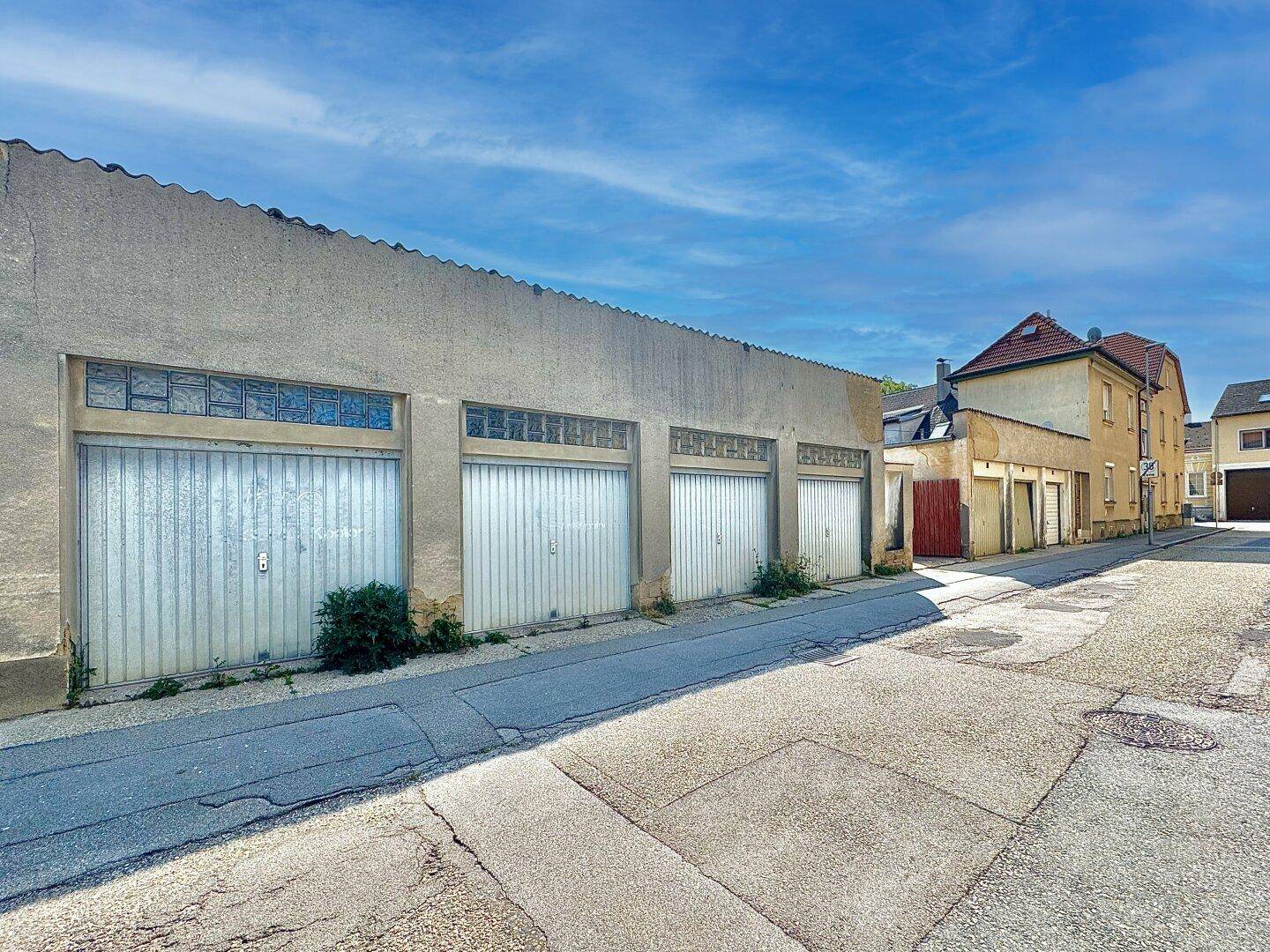 Reihe von Garagen oder Lagerhallen entlang der Straße, mit dem Hauptgebäude im Hintergrund sichtbar.