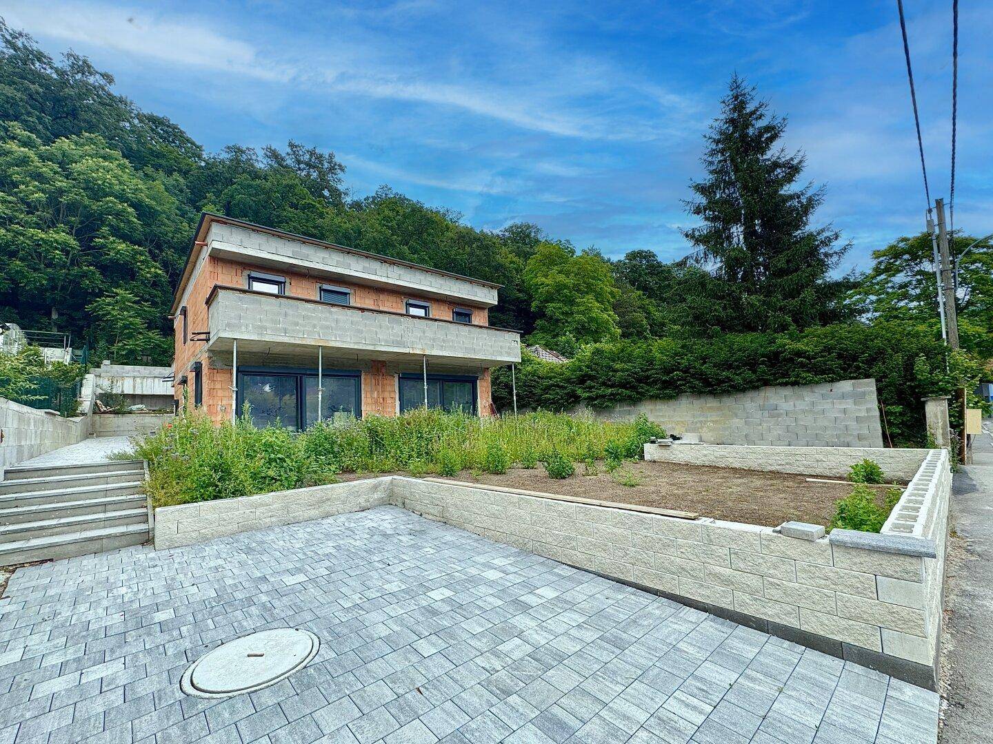 Neubau-Einfamilienhaus mit moderner Architektur, großzügigen Fenstern und Balkon, umgeben von Natur.