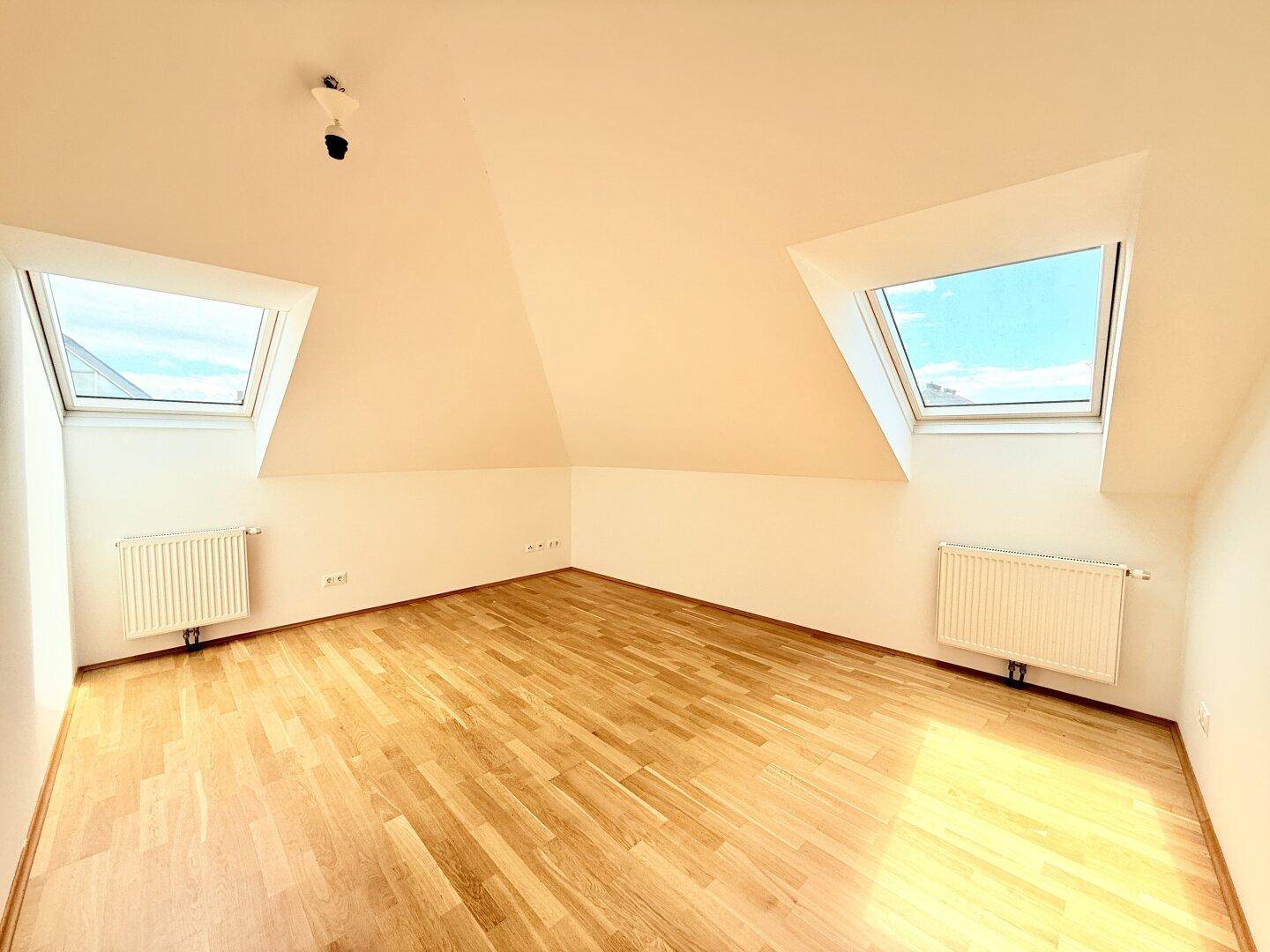 Geräumiges Dachzimmer mit zwei großen Dachfenstern und hellem Parkettboden, ideal für ein Schlafzimmer.