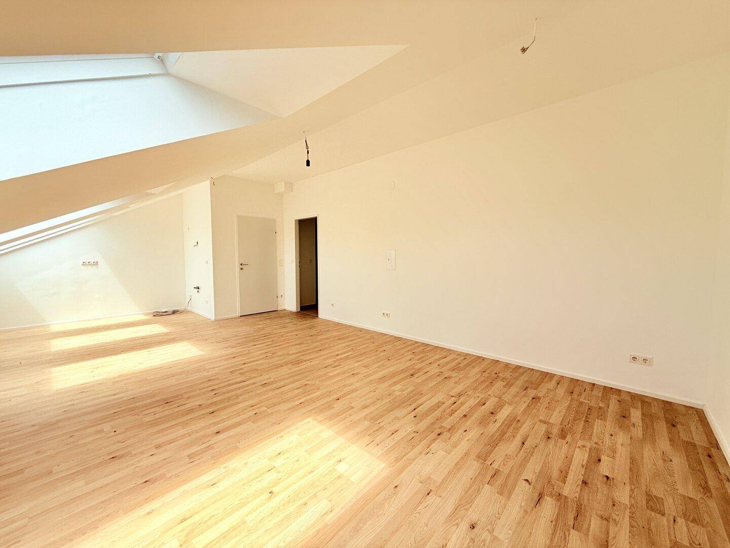Lichtdurchfluteter Raum im Dachgeschoss mit Schrägdecke, Parkettboden und Zugang zu weiteren Räumen.