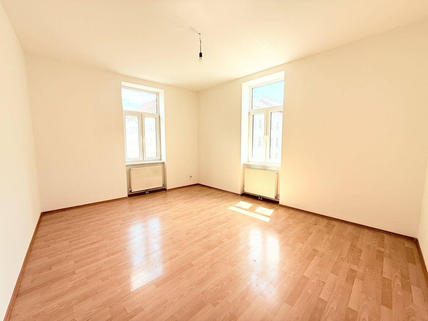 Heller Raum mit zwei großen Fenstern, Parkettboden und Heizkörpern, bietet viel Tageslicht.