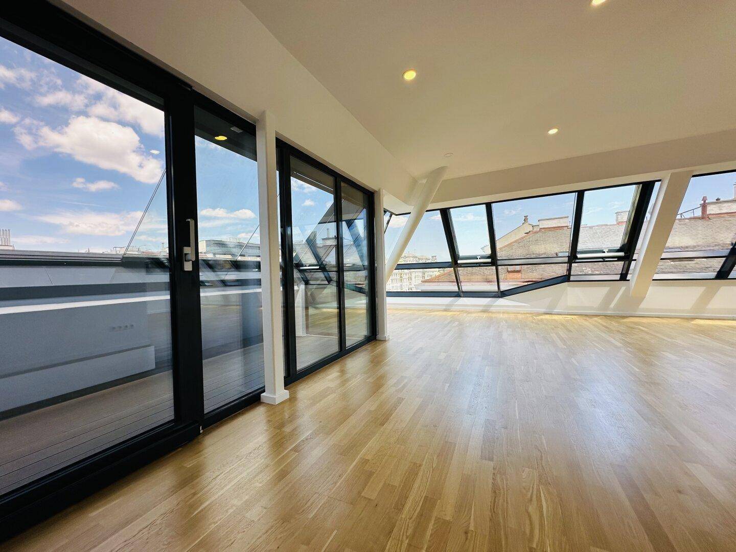 Heller, geräumiger Wohnbereich mit Holzboden, großen Fenstern und Zugang zu einem Balkon mit Stadtblick.