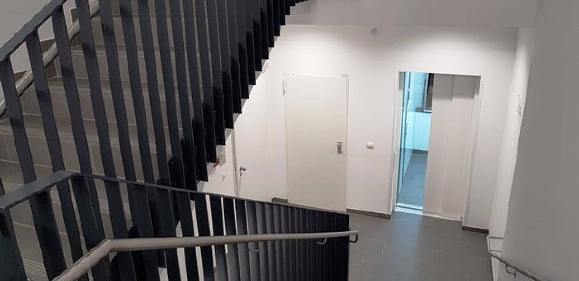 Geräumiges Treppenhaus mit dunklem Geländer und Fliesenboden, führt zu weiteren Etagen.