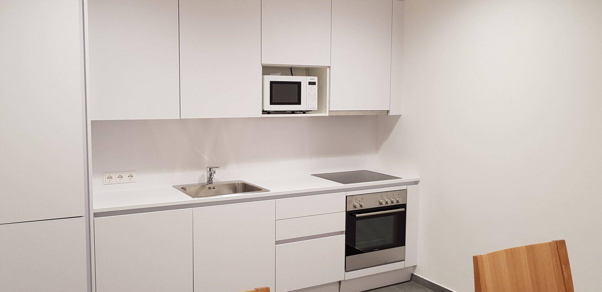 Moderne, weiße Küchenzeile mit integriertem Backofen, Induktionskochfeld und Mikrowelle.