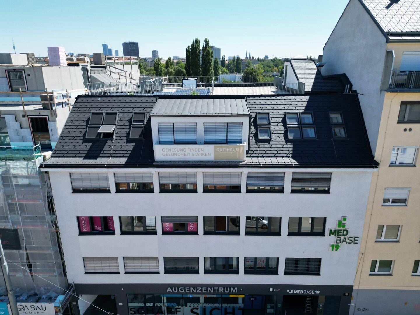 Gebäudeansicht von vorne mit Geschäften im Erdgeschoss und Büros darüber, umgeben von städtischer Bebauung.