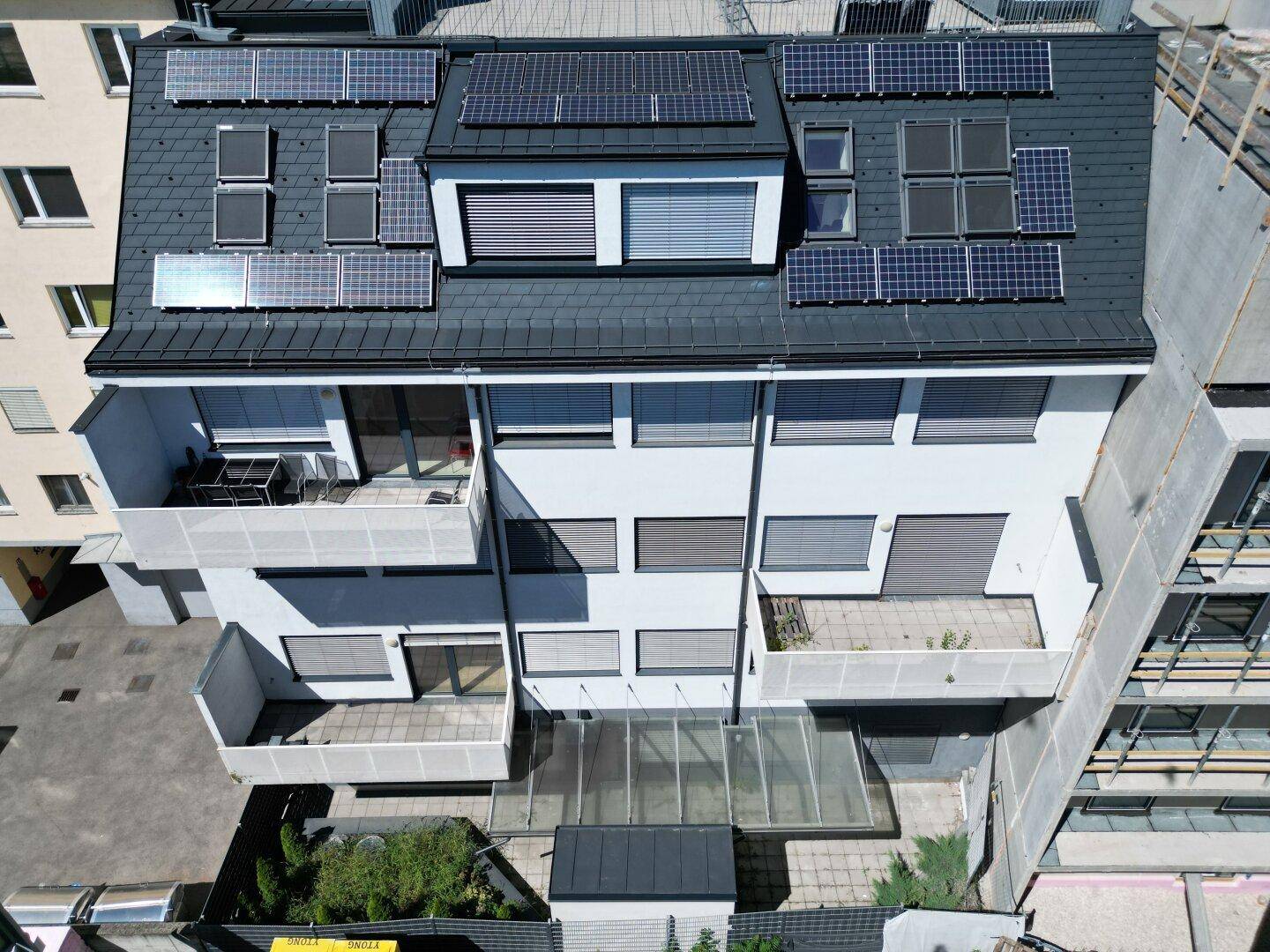Dachansicht eines Gebäudes mit Photovoltaikanlage und mehreren Balkonen an der Rückseite.