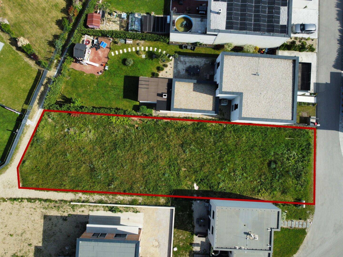 Luftaufnahme eines Baugrundstücks mit roter Umrandung, umgeben von modernen Wohnhäusern und Grünflächen.