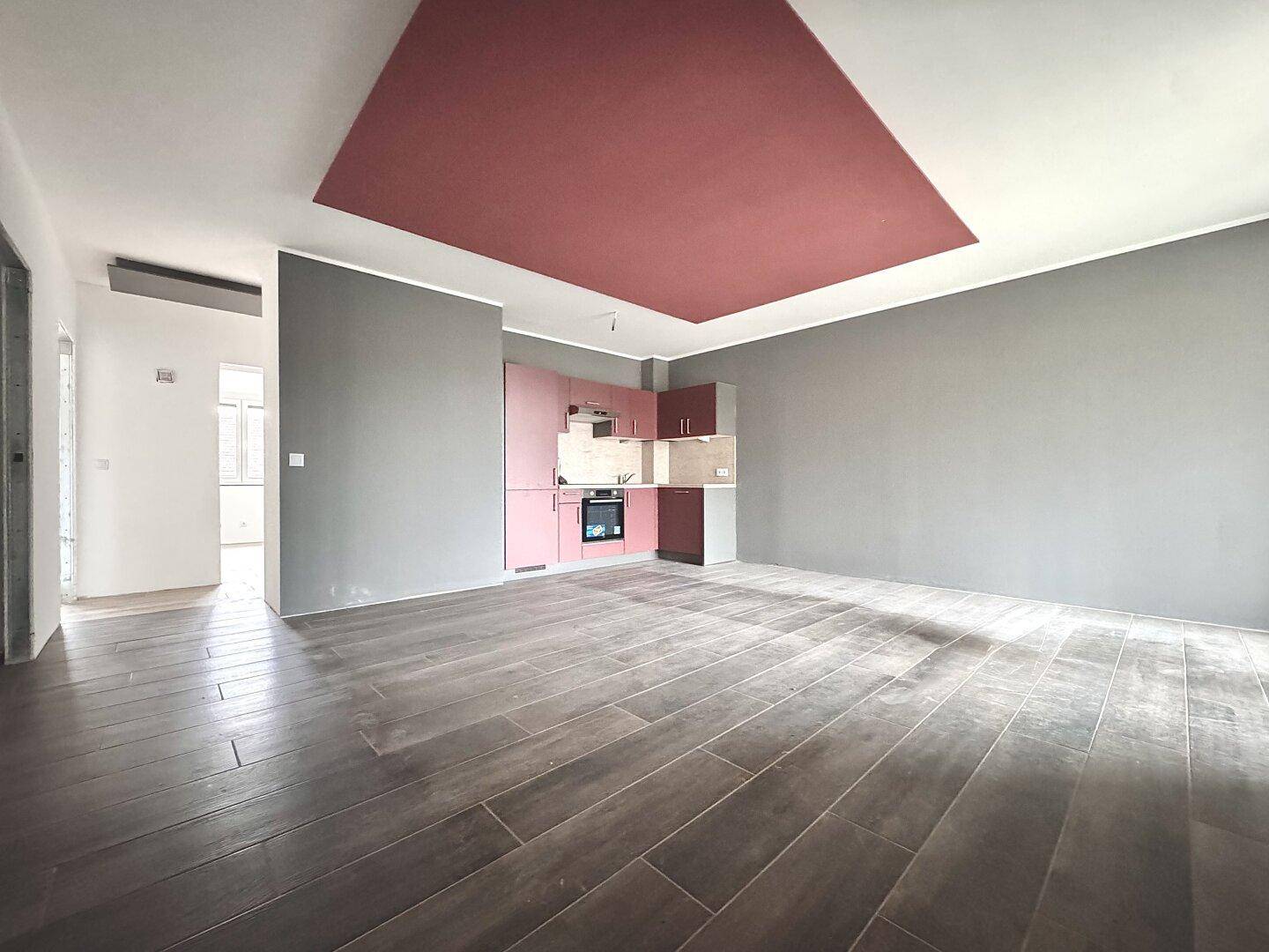 Geräumiger Wohnbereich mit integrierter Küchenzeile, modernem Fliesenboden und farbiger Decke.