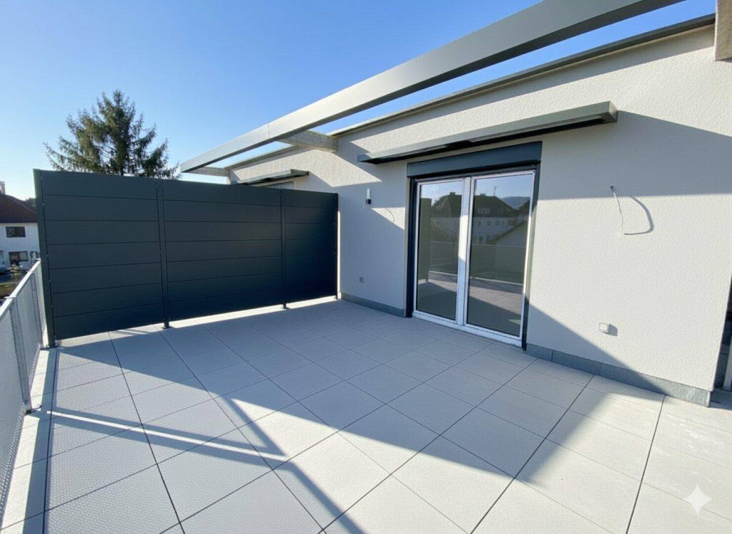Große Dachterrasse mit modernen Fliesen und Sichtschutz, ideal für Entspannung im Freien.