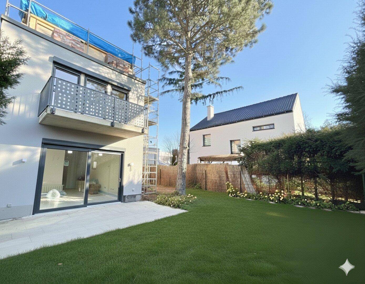 Rückseite eines modernen Hauses mit Balkon, großer Glasschiebetür und einer grünen Rasenfläche.