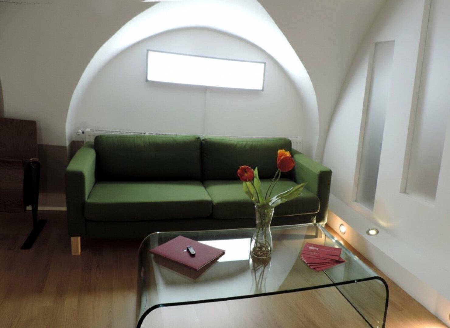 Gemütliches Wohnzimmer mit modernem grünem Sofa, elegantem Glastisch und einzigartiger Gewölbedecke, ergänzt durch stilvolle Beleuchtung.