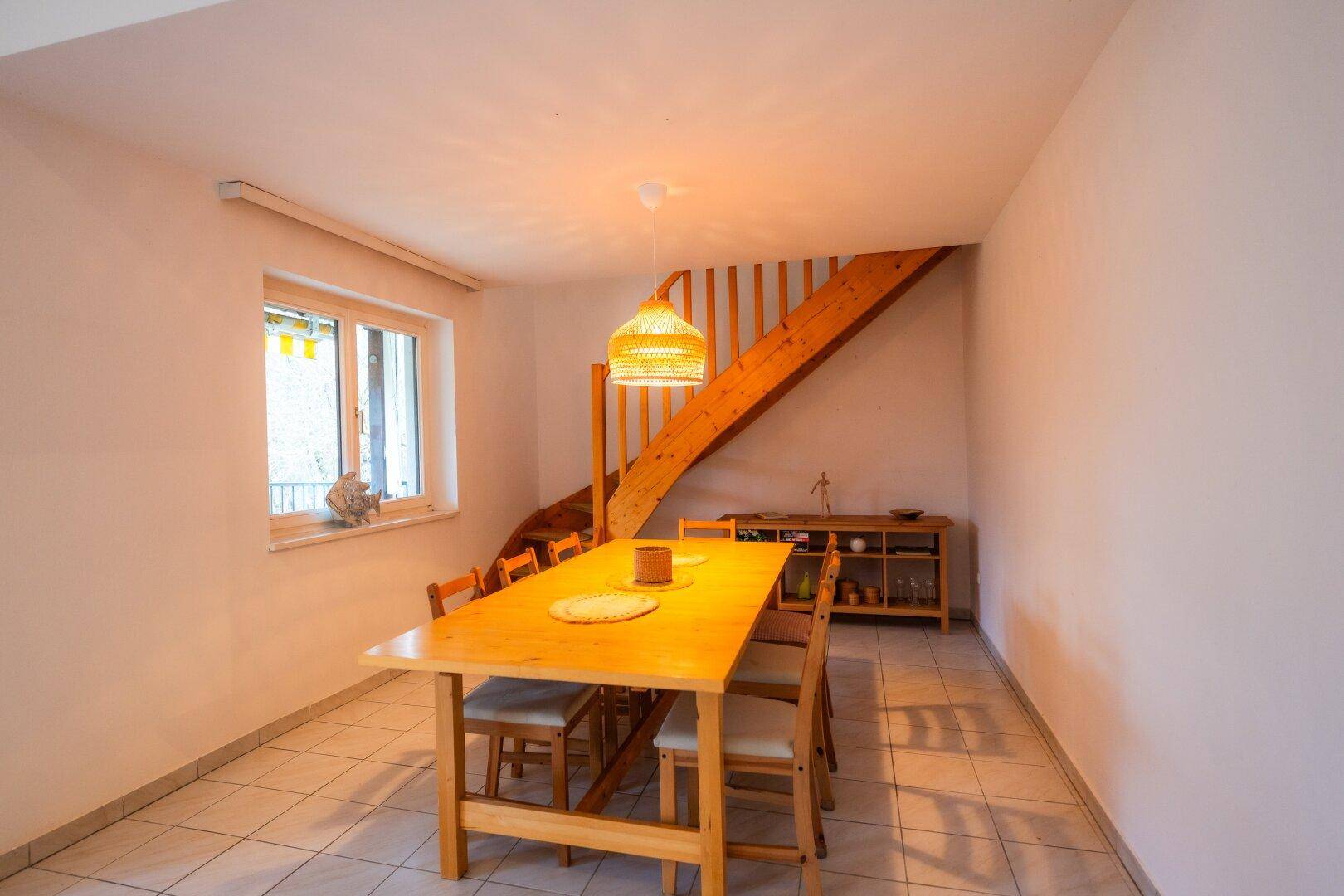 Gemütlicher Essbereich mit Holztisch, Stühlen und einer offenen Holztreppe in hellem Raum.