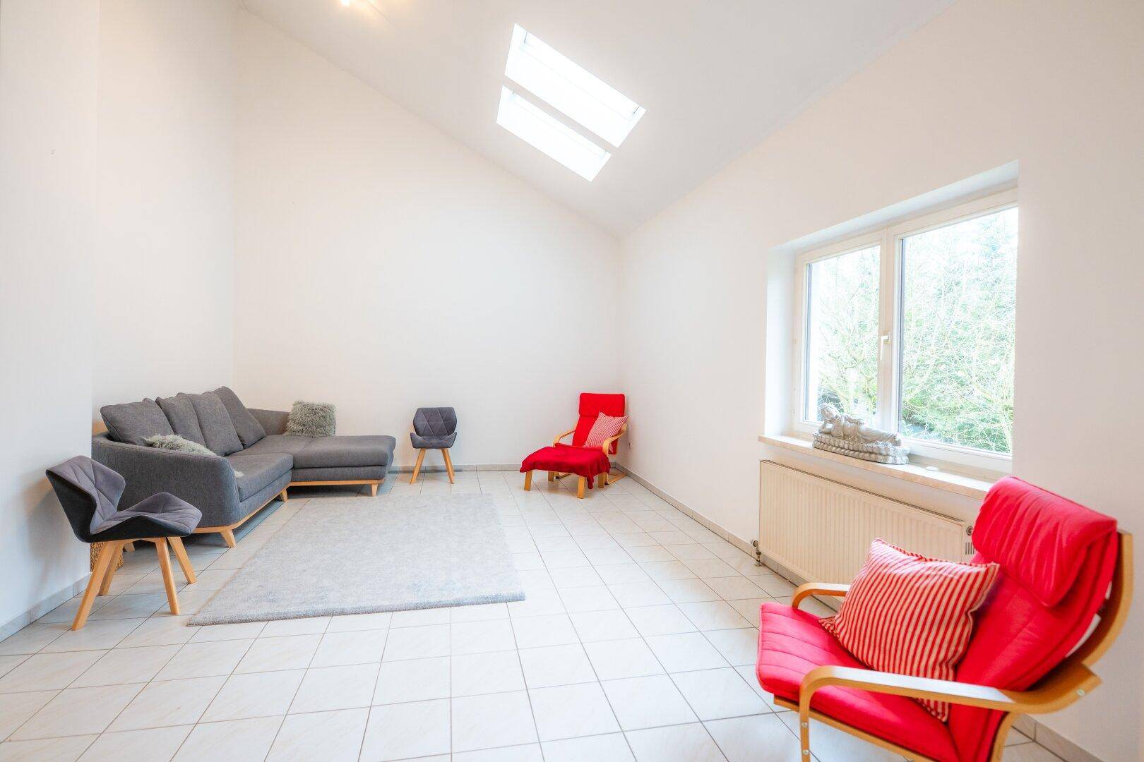 Geräumiges Wohnzimmer mit Fliesenboden, Dachfenstern und moderner Sitzgruppe in hellem Ambiente.