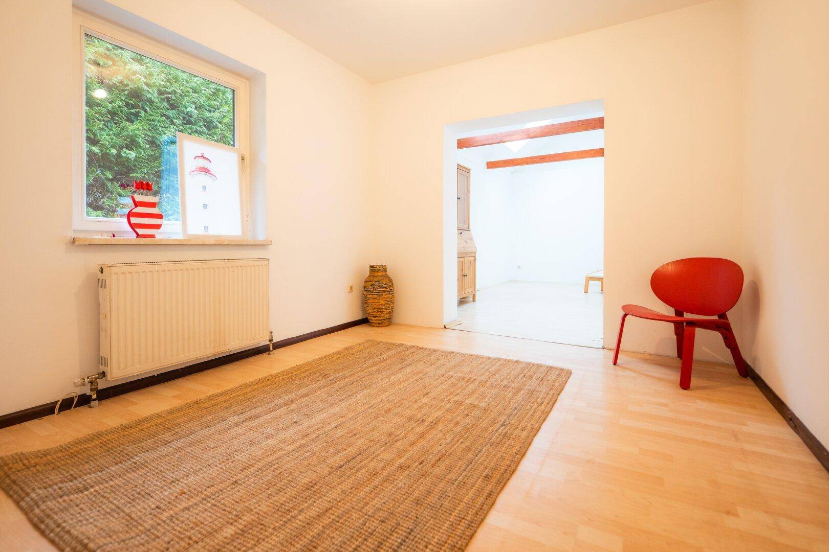 Heller Raum mit Holzboden, großem Fenster und einem angenehmen Blick ins Grüne.