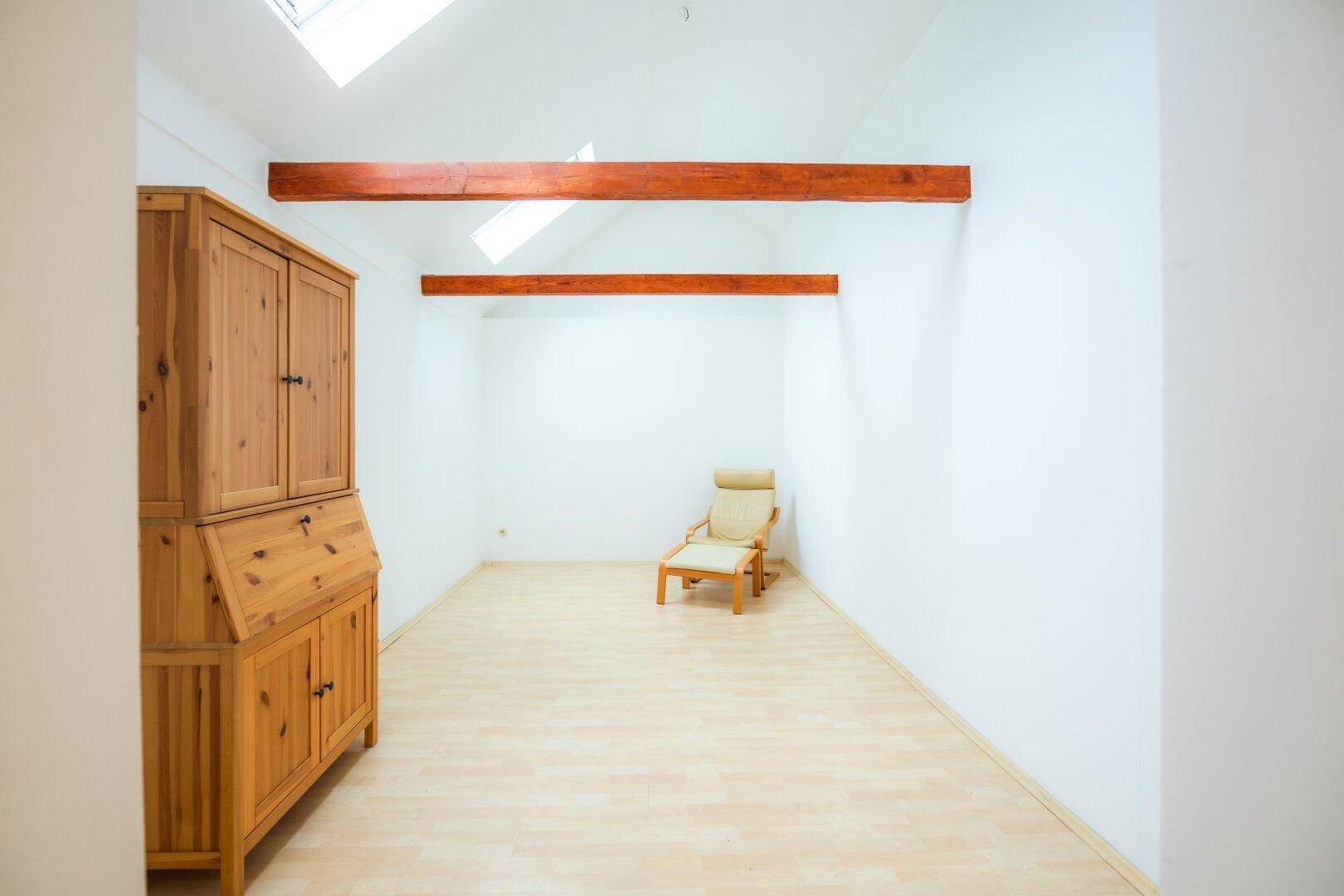 Dachgeschosszimmer mit sichtbaren Holzbalken, Dachfenstern und hellem Holzboden.