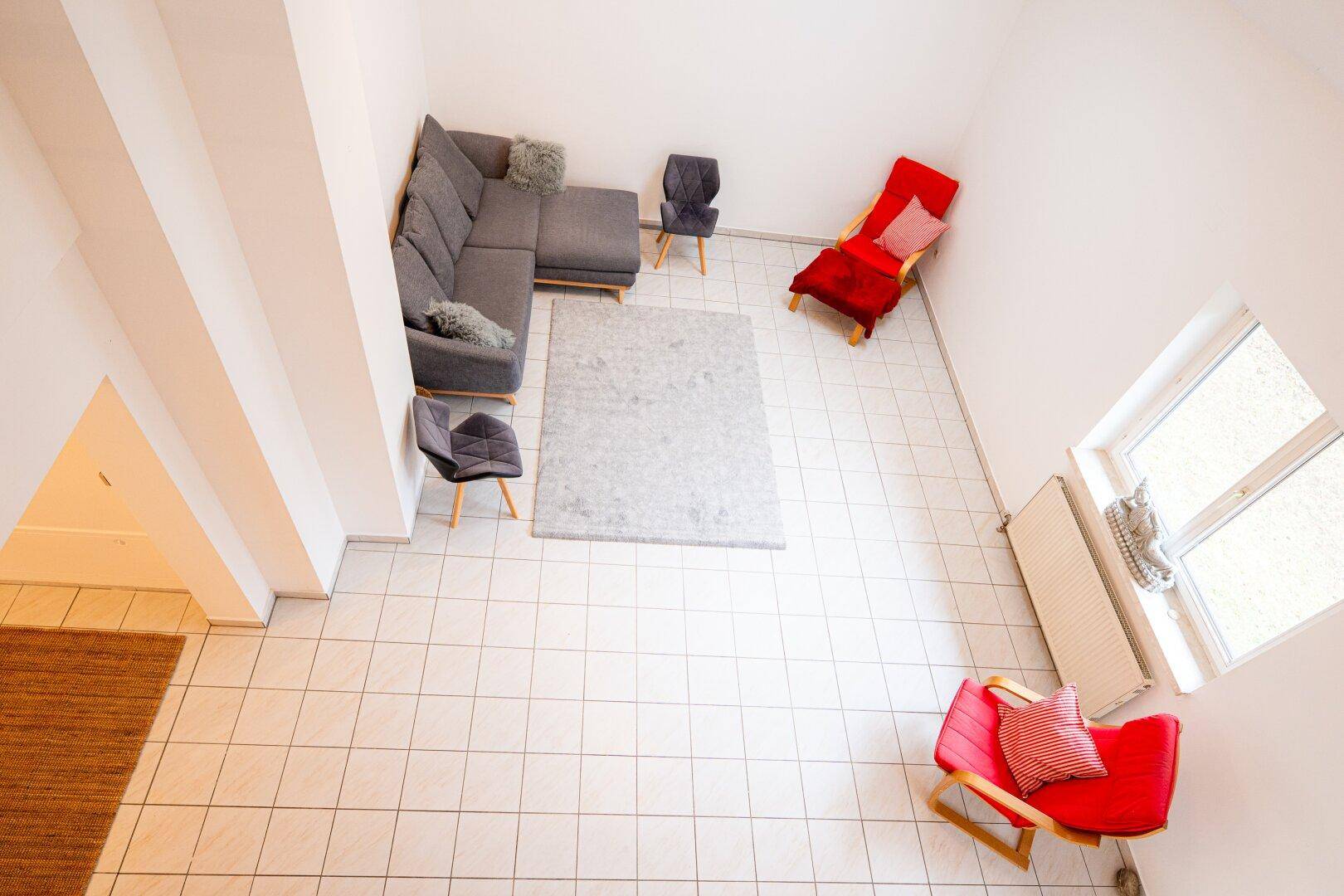 Vogelperspektive des Wohnzimmers mit Fliesenboden, Dachfenstern und moderner Sitzgruppe.